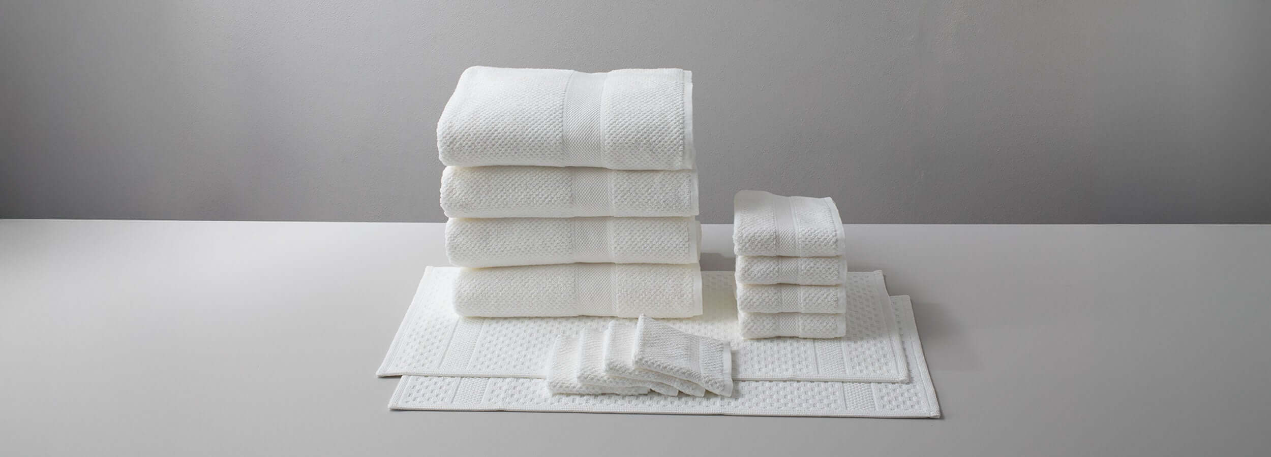 Stacked white towels on a light gray surface, showcasing plush bath linens and matching accessories.