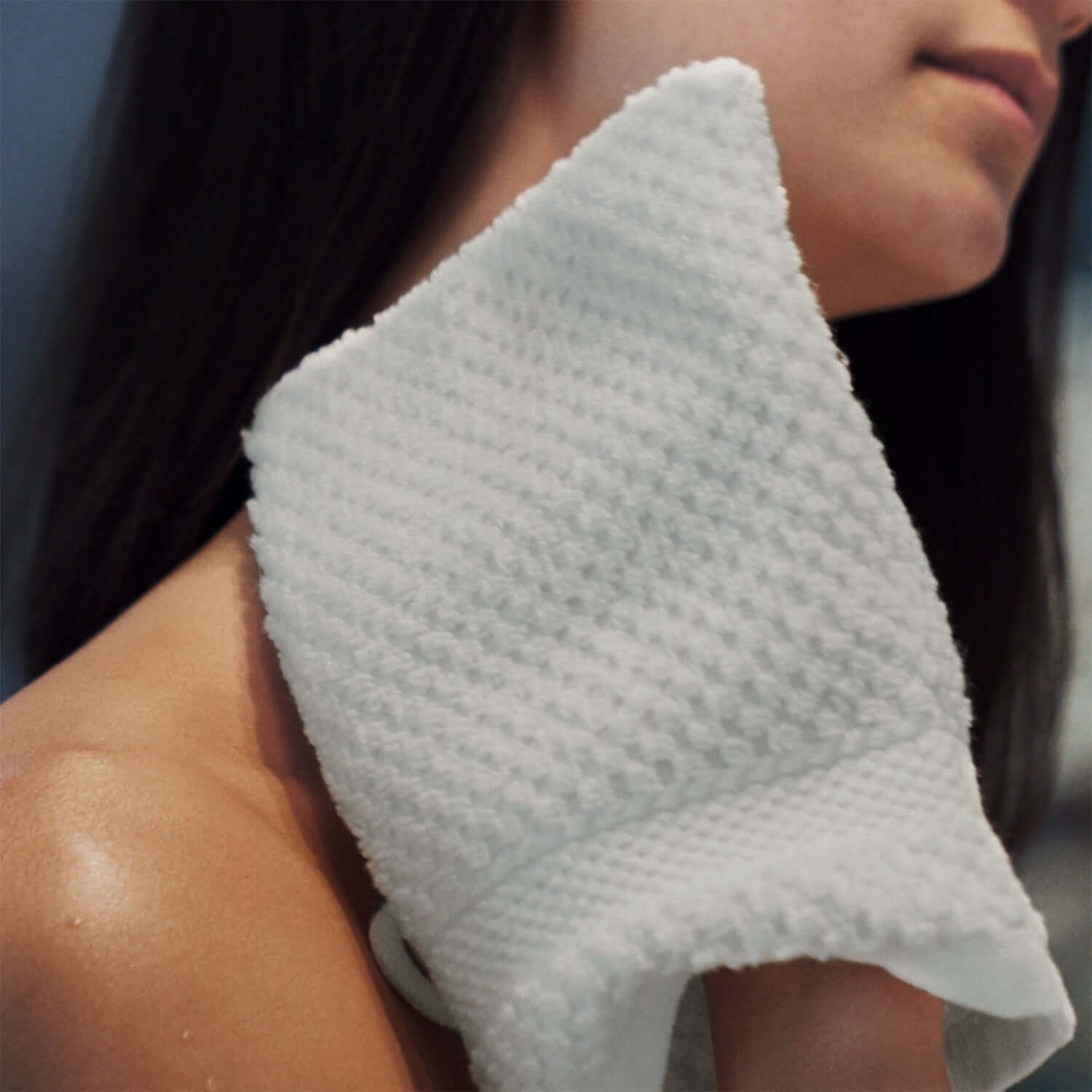 Close-up of a woman patting her skin with a fluffy white Novotel Glove for gentle exfoliation after a body wash.