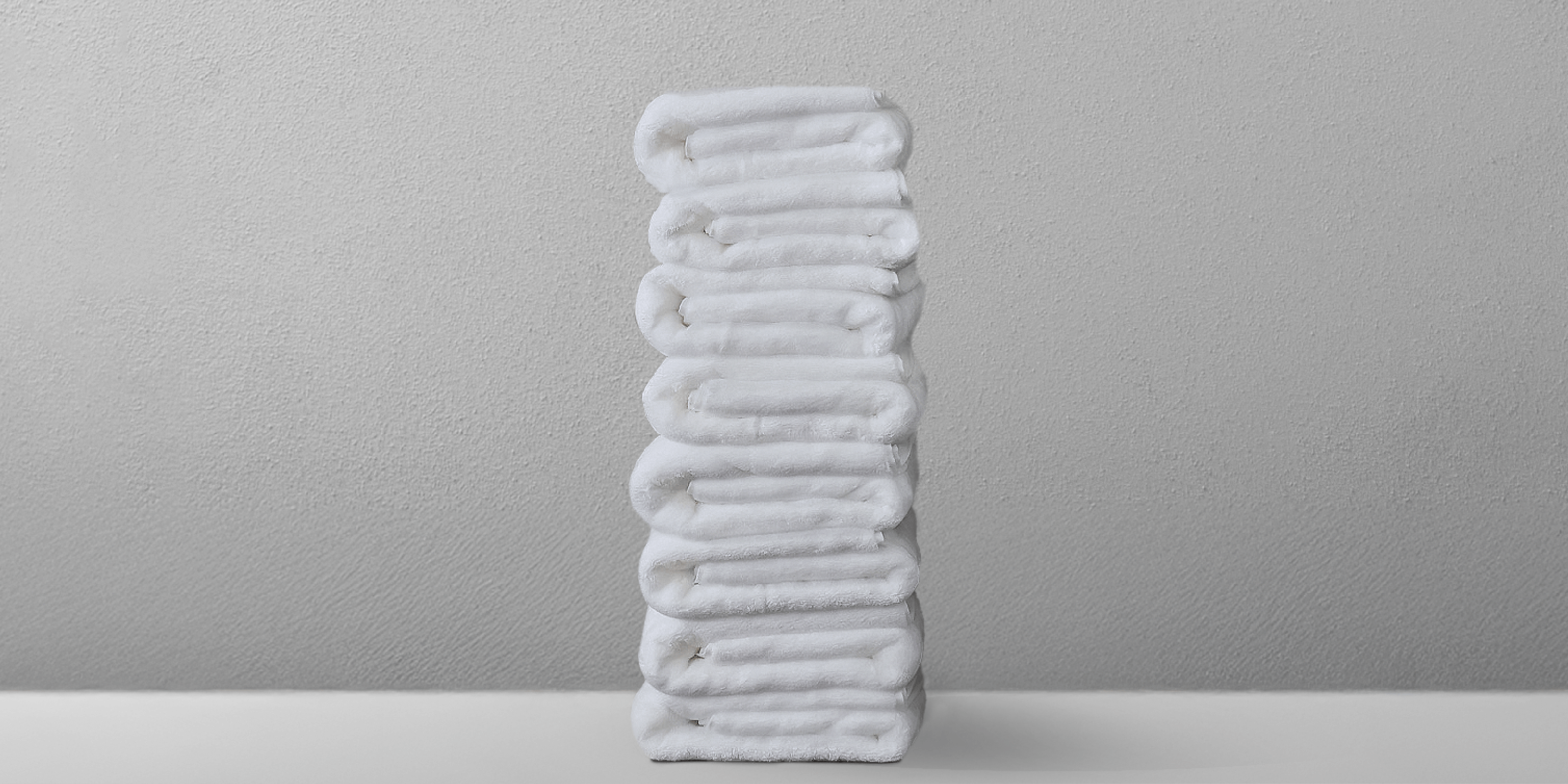 Stack of neatly folded white towels on a light surface against a gray background.