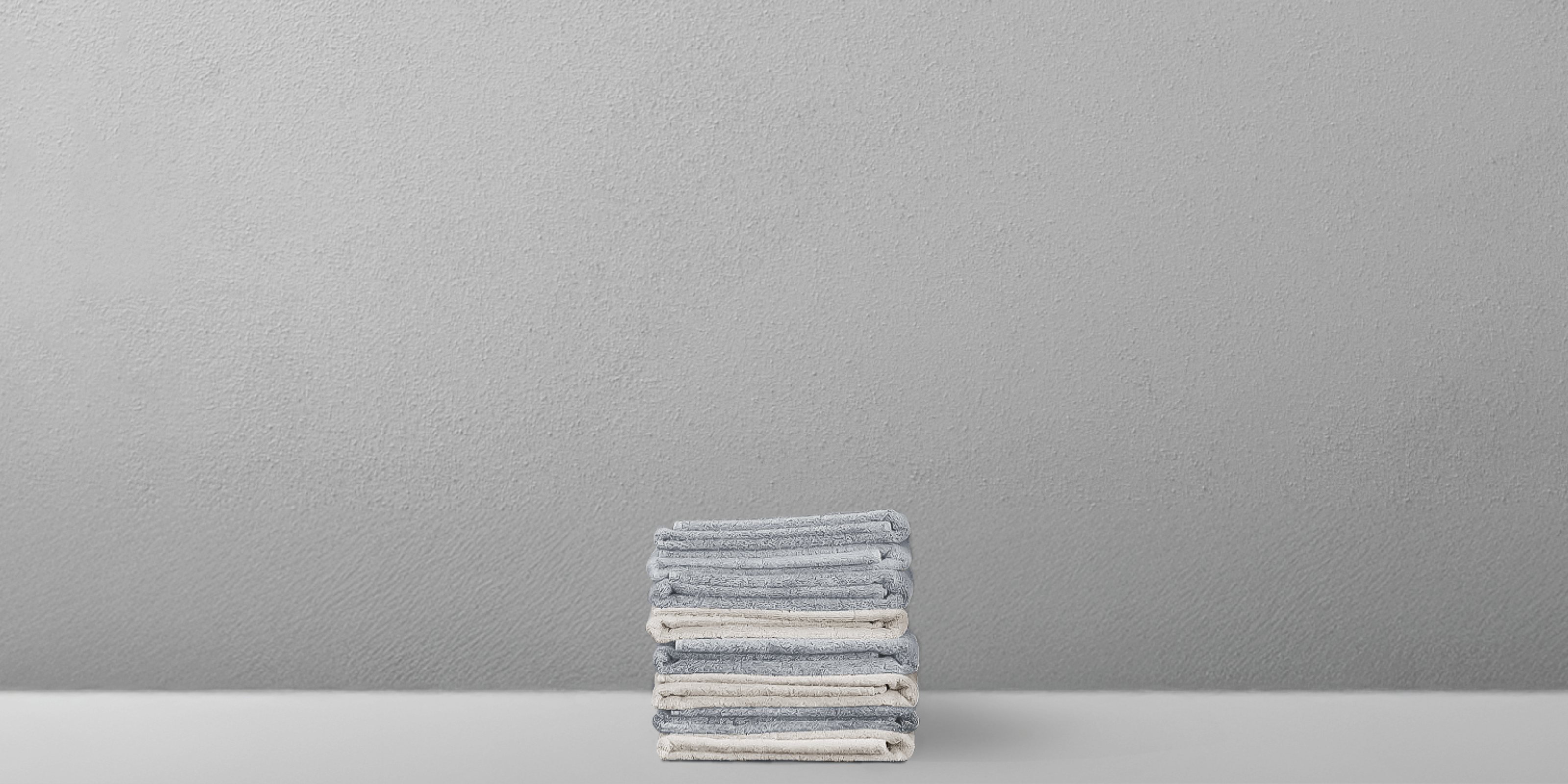 Neatly stacked grey towels on a minimalist white shelf against a textured grey wall.