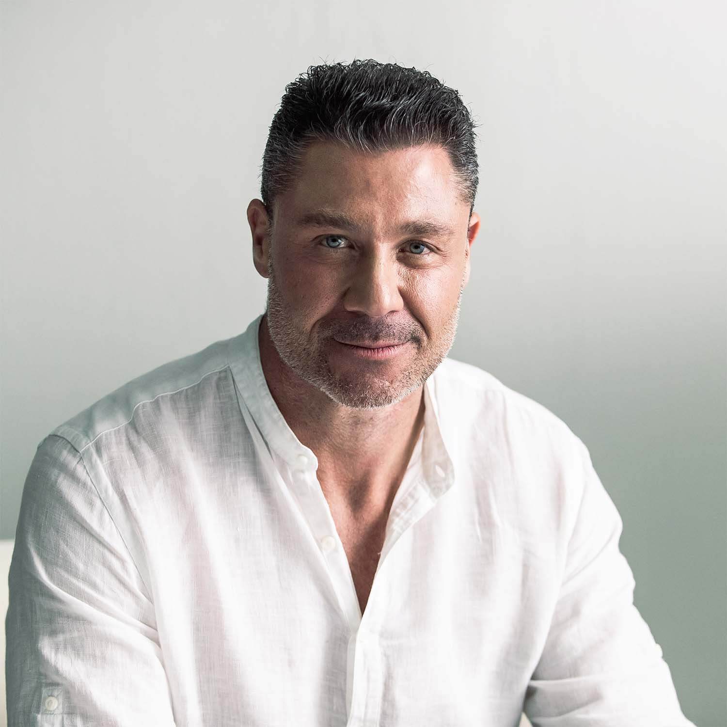 Professional portrait of a man in a white shirt, conveying confidence and approachability in a serene background.