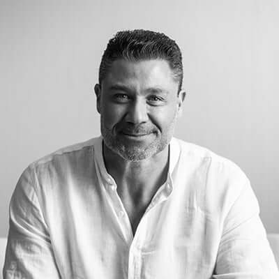 Portrait of a smiling man in a white shirt, against a light background, exuding confidence and warmth.