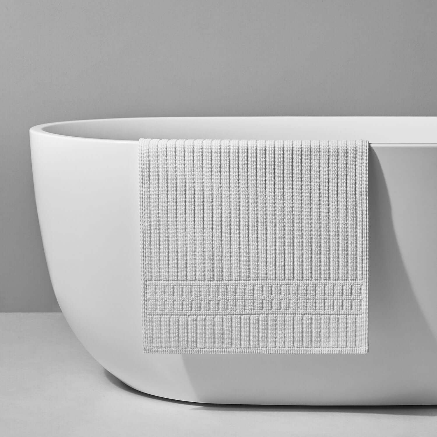 Textured white towel draped over a sleek, modern bathtub, showcasing luxury and elegance in bathroom decor.