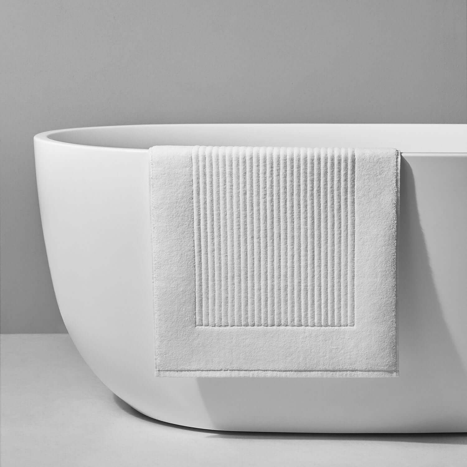 White velour bath mat with ribbed texture draped over a modern freestanding bathtub.