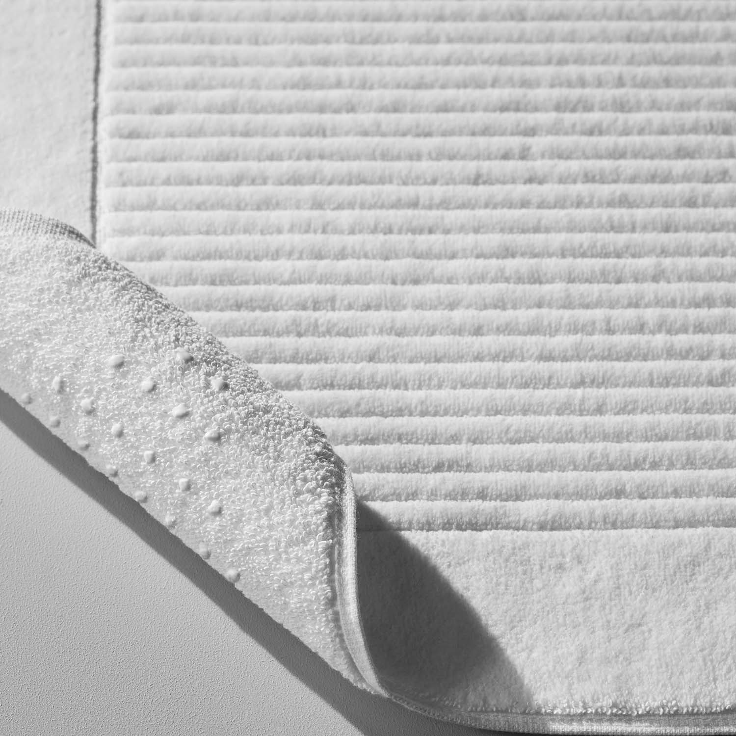 Close-up of luxurious white cotton velour mat showcasing textured surface and Slip-Less© technology for safety.