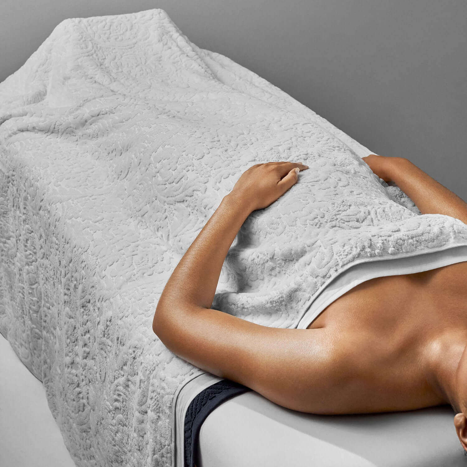 Luxurious white Baroque blanket draped over a relaxing figure, showcasing its soft velour texture and elegant pattern.