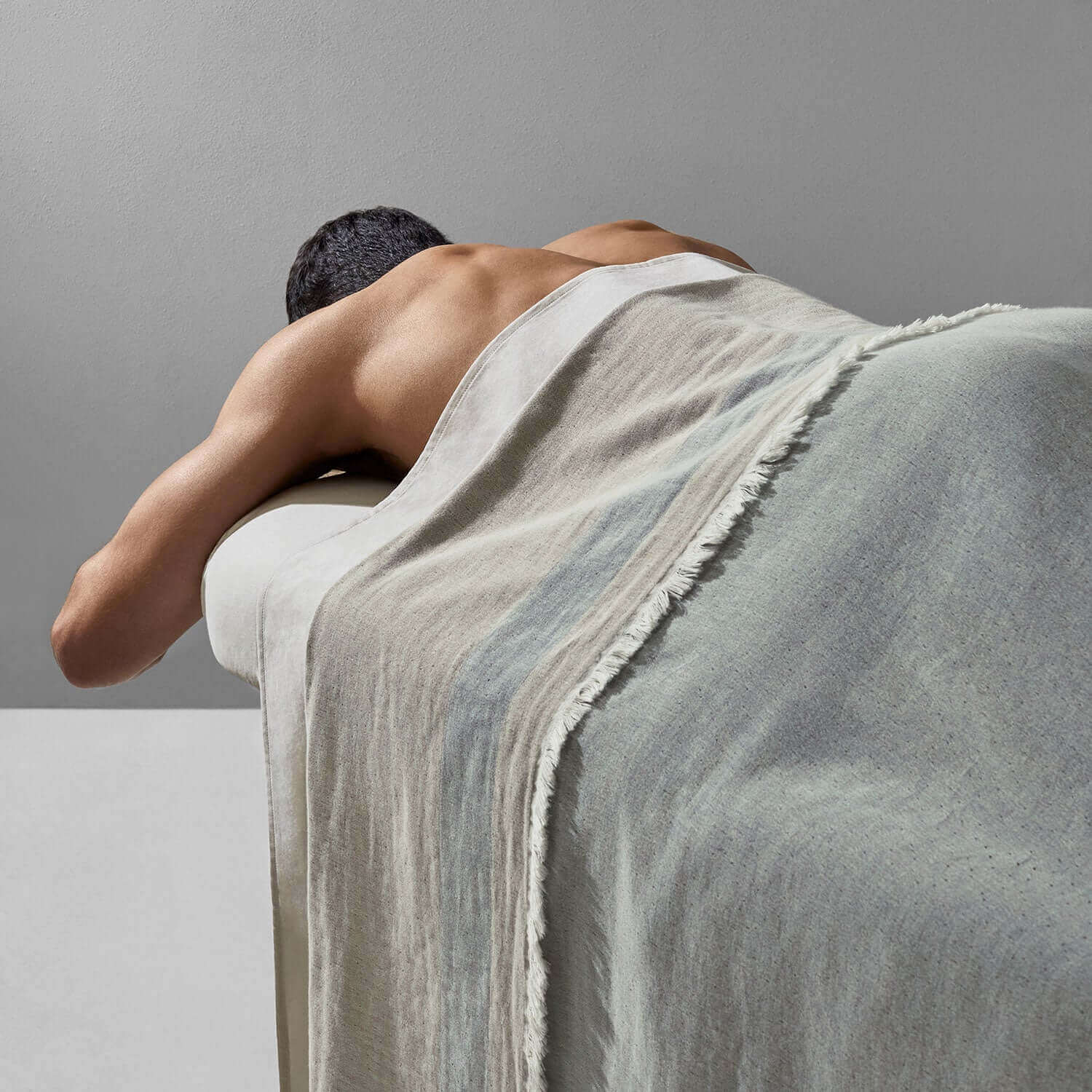 Man relaxing with a Cenote Blanket, showcasing its two-toned, three-layered design for spa and wellness use.