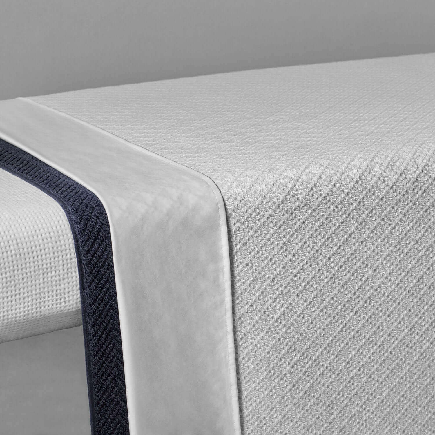 Lightweight cotton blanket with a textured white weave and navy double-wide hem, ideal for hotels and resorts.