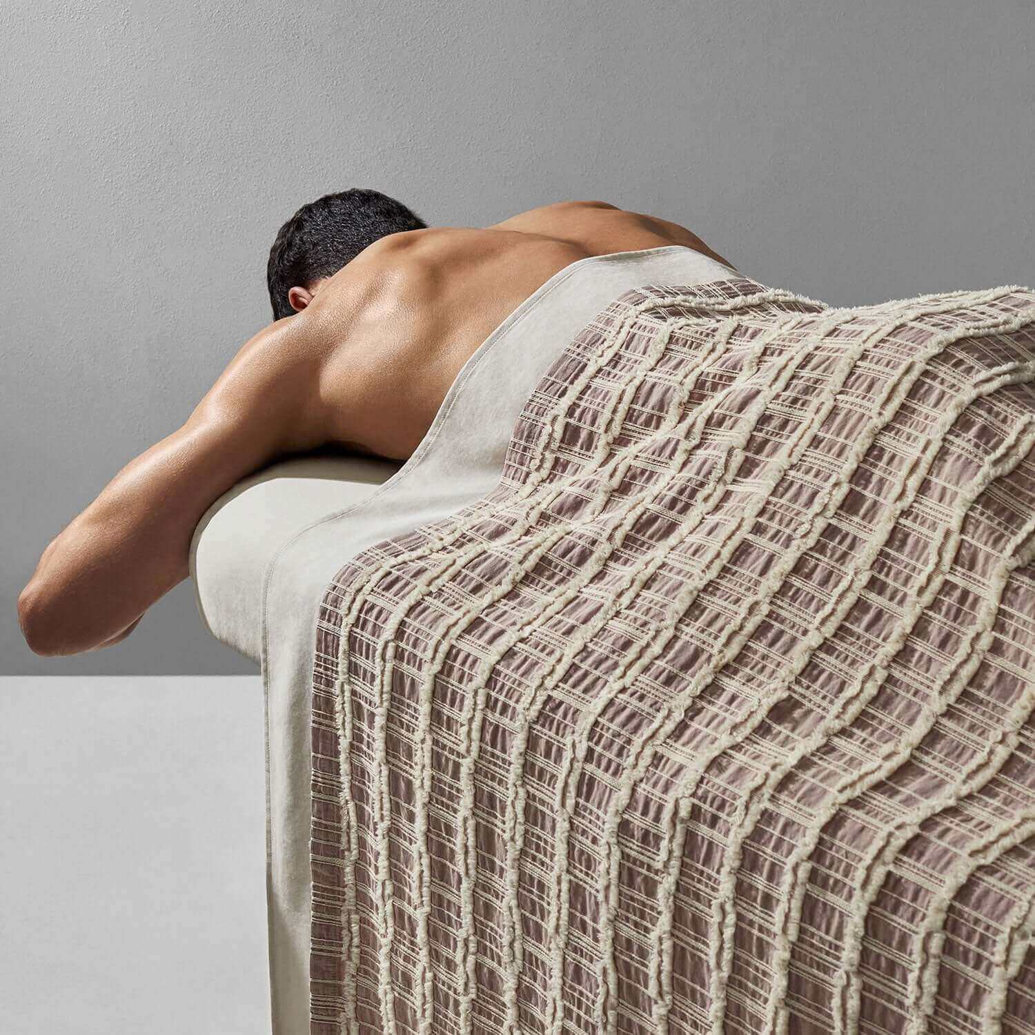 Lattice blanket in light rose and salmon colors draped over a massage table with a relaxed model.