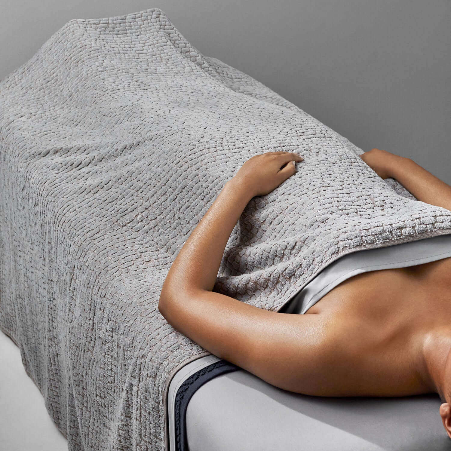 Gray pebble blanket draped over a client on a spa table, showcasing its softness and natural texture.