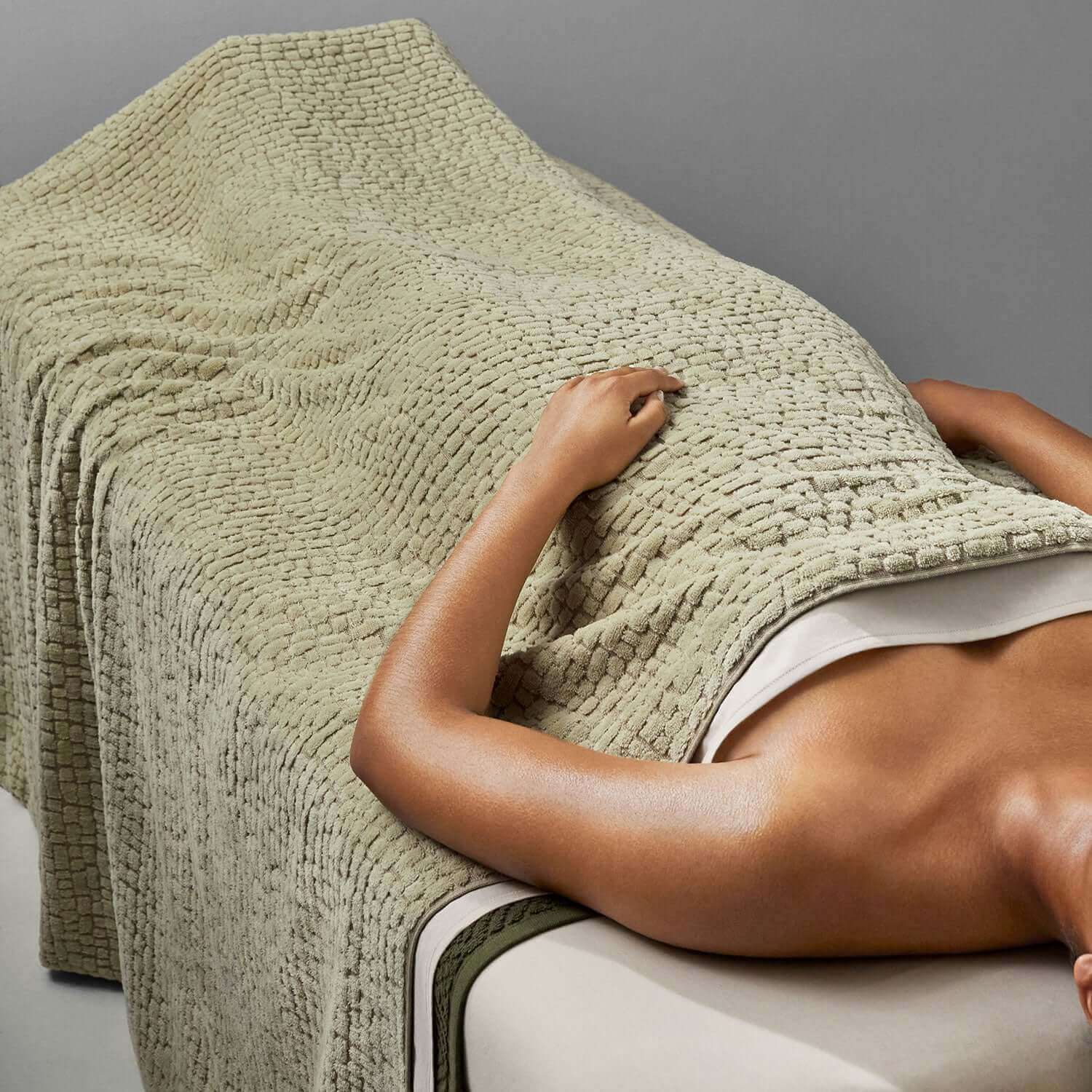 Sage pebble blanket covering a person on a massage table, showcasing natural softness and luxurious texture.