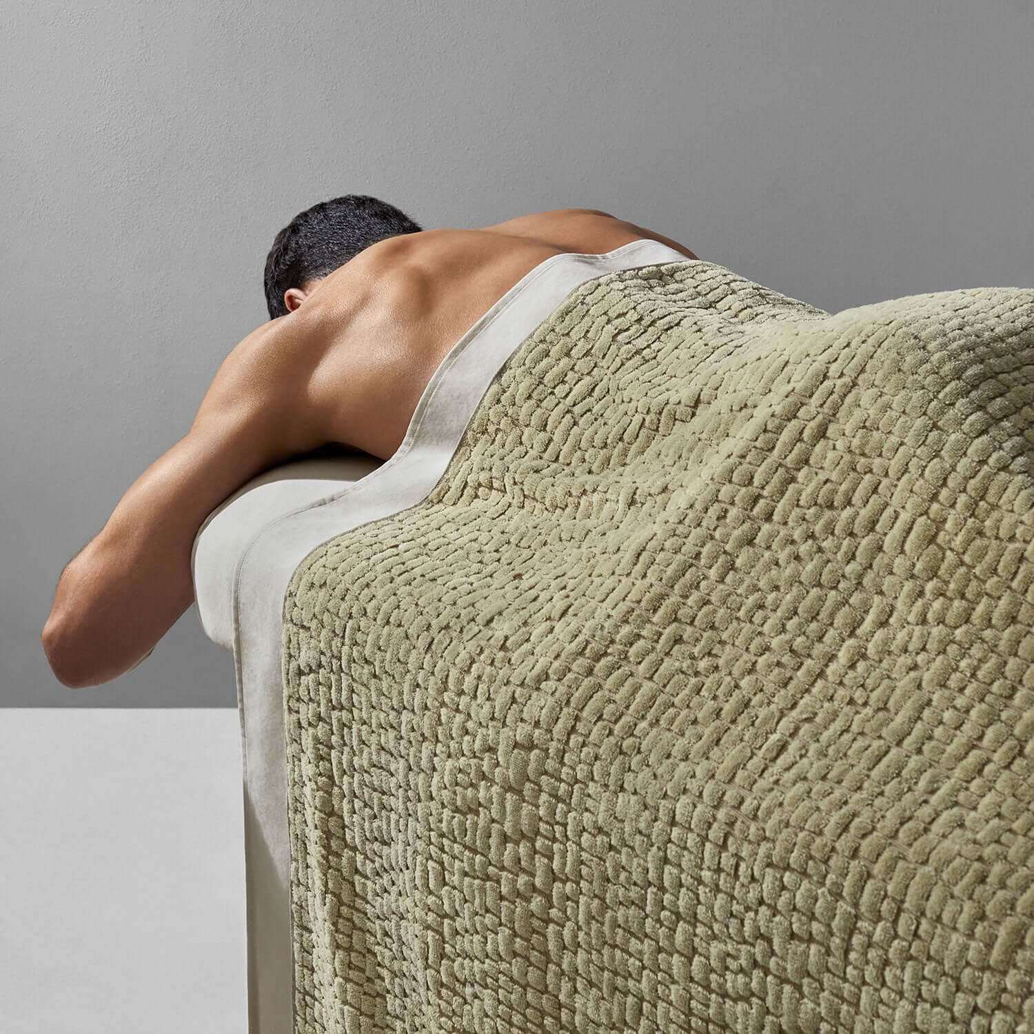 A person receiving a massage covered with a sage pebble blanket, showcasing its softness and luxurious design.