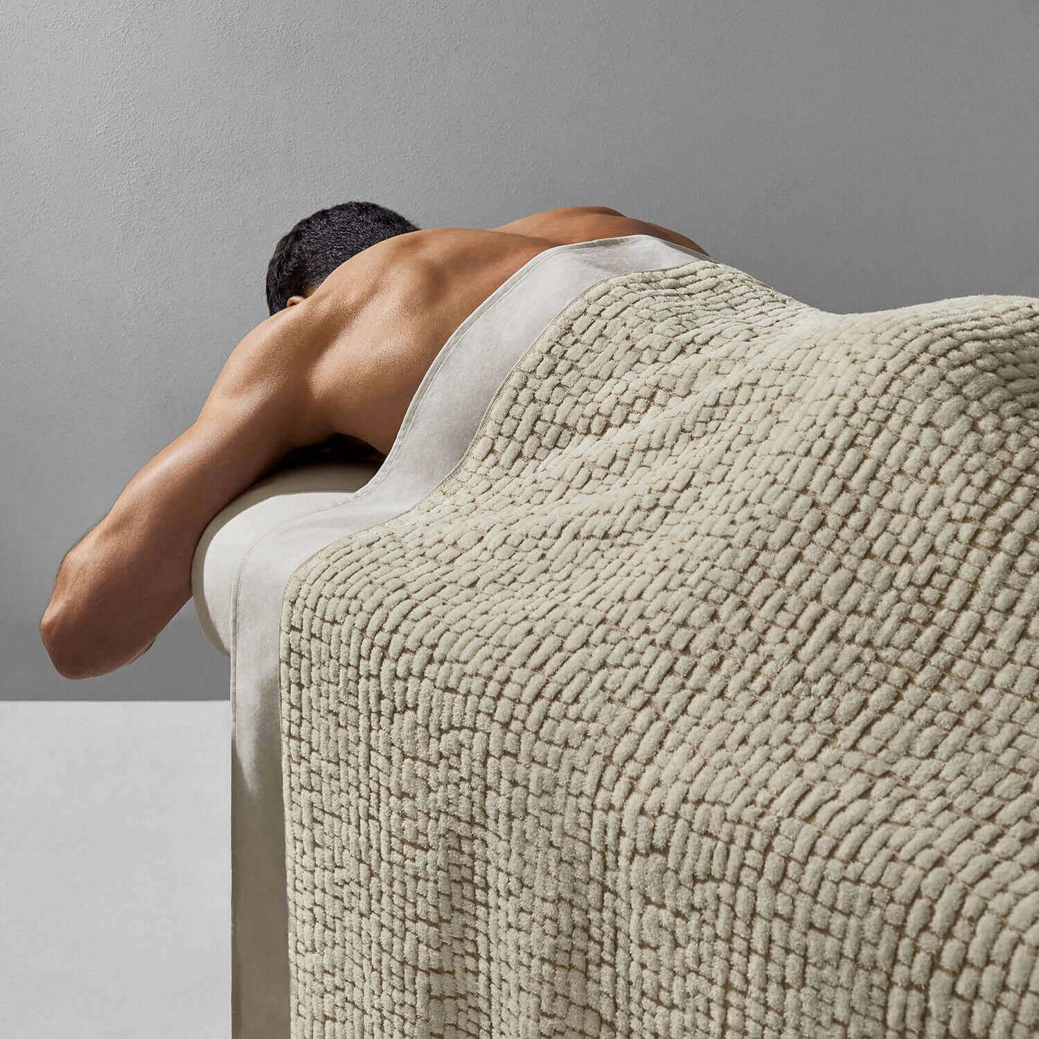 Individual enjoying a massage with a soft Pebble Blanket Sand on a treatment table, highlighting spa relaxation.