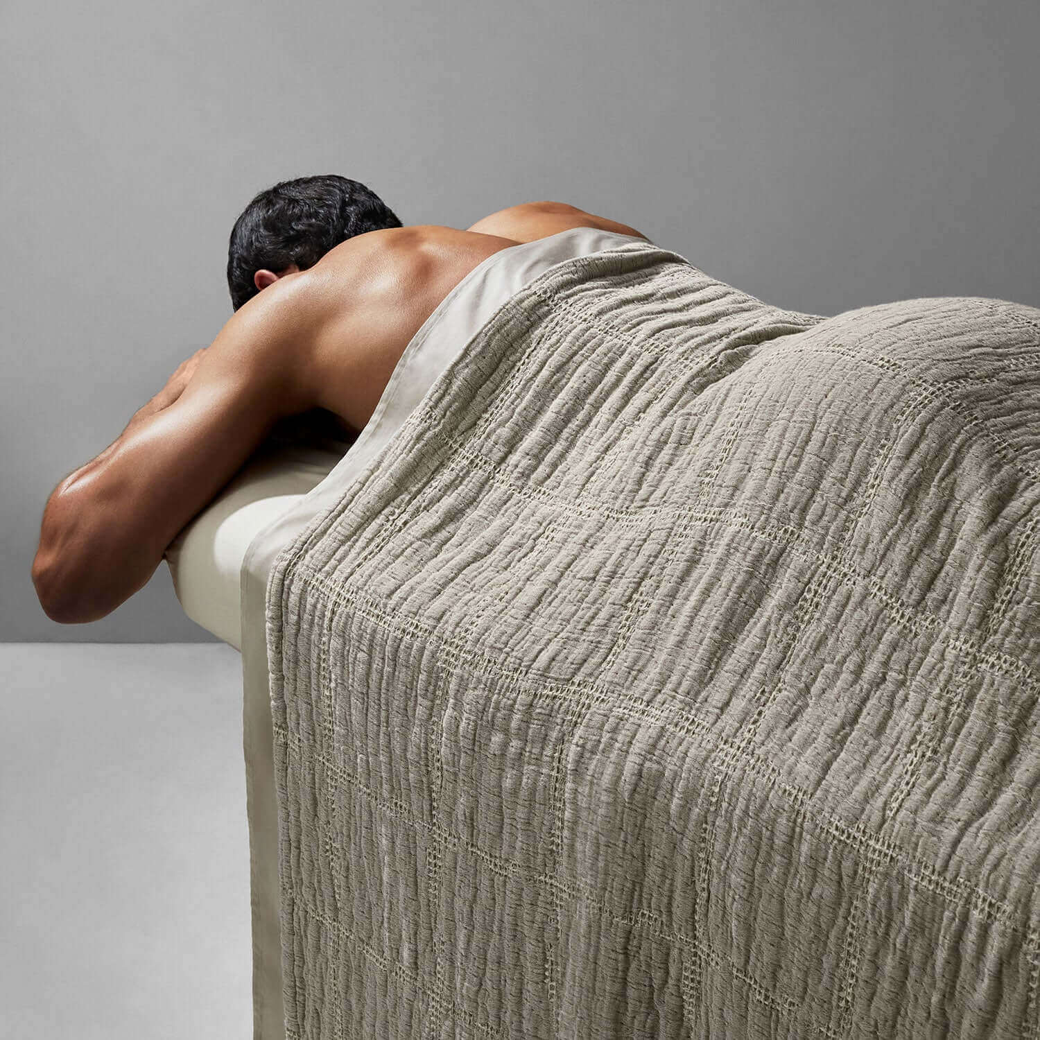 Person relaxing under a soft stone-beige stitch blanket, showcasing its textured cotton and rustic charm.