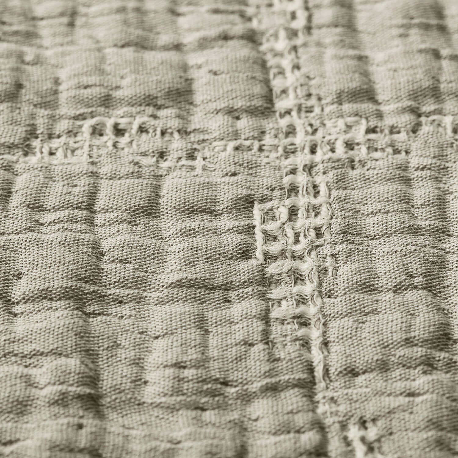 Close-up of textured stone-beige cotton stitch blanket, showcasing unique stitching details and rustic elegance.