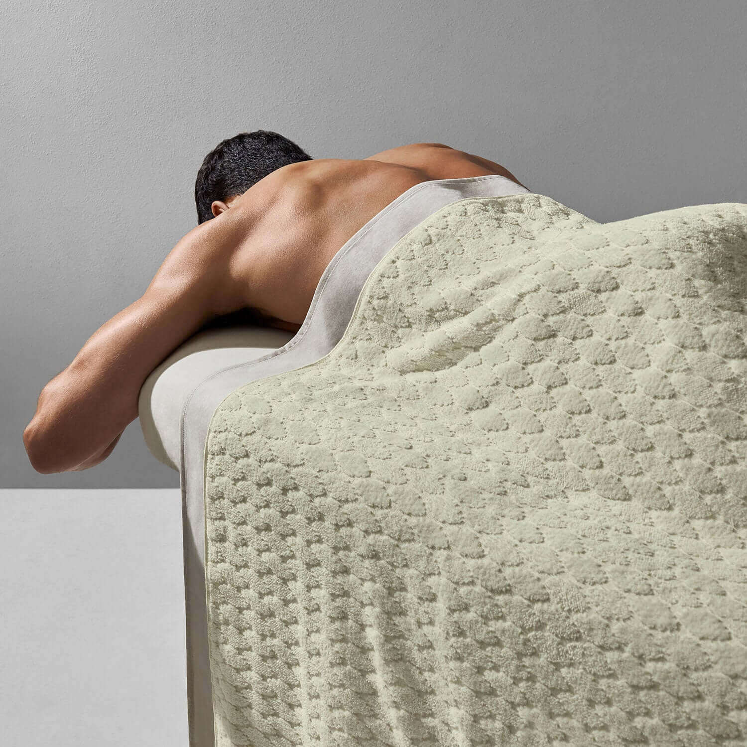 A man enjoying a relaxing massage, covered with a soft velour blanket in a soothing natural color.