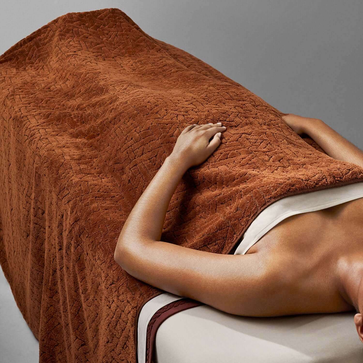 Wabi Sabi blanket in warm brown covering a person on a massage table, showcasing minimalist design and luxury.