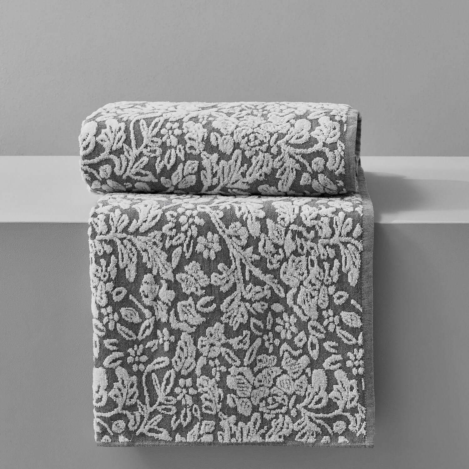 Luxury grey and white floral jacquard towels stacked on a display, showcasing intricate yarn-dyed design.