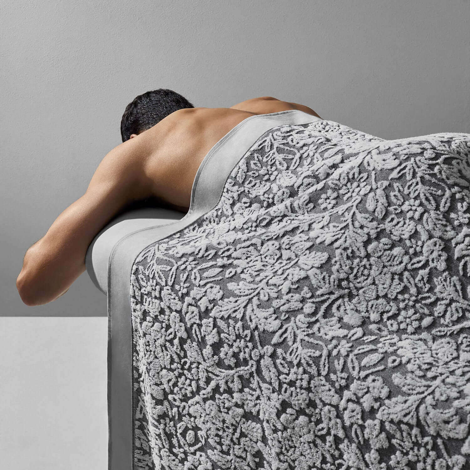 Man wrapped in a luxurious yarn-dyed grey and white blanket, showcasing intricate jacquard weave craftsmanship.