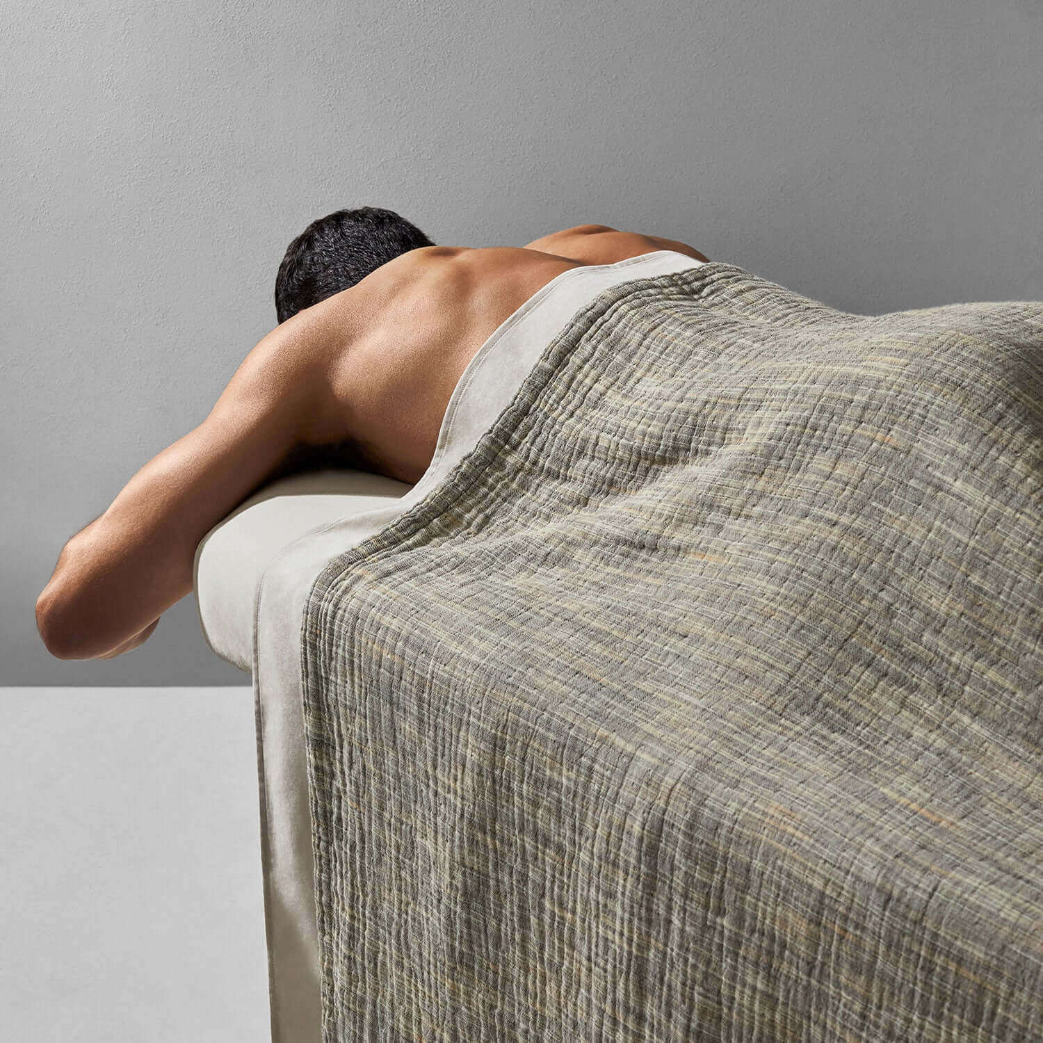 A man receiving a massage while covered with a printed yarn blanket on a spa treatment table.