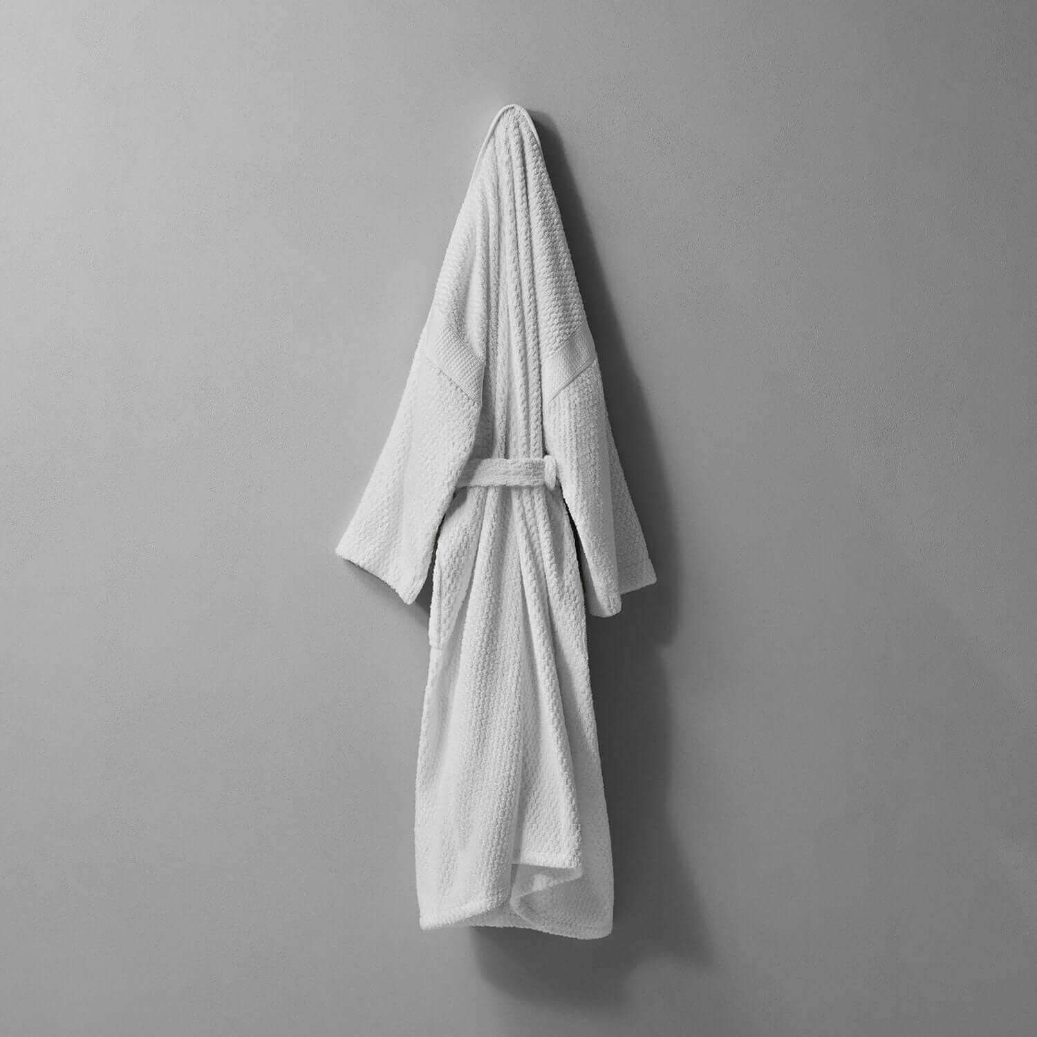 White kimono robe with braided neckline and statement sleeves, draped elegantly against a simple gray wall.