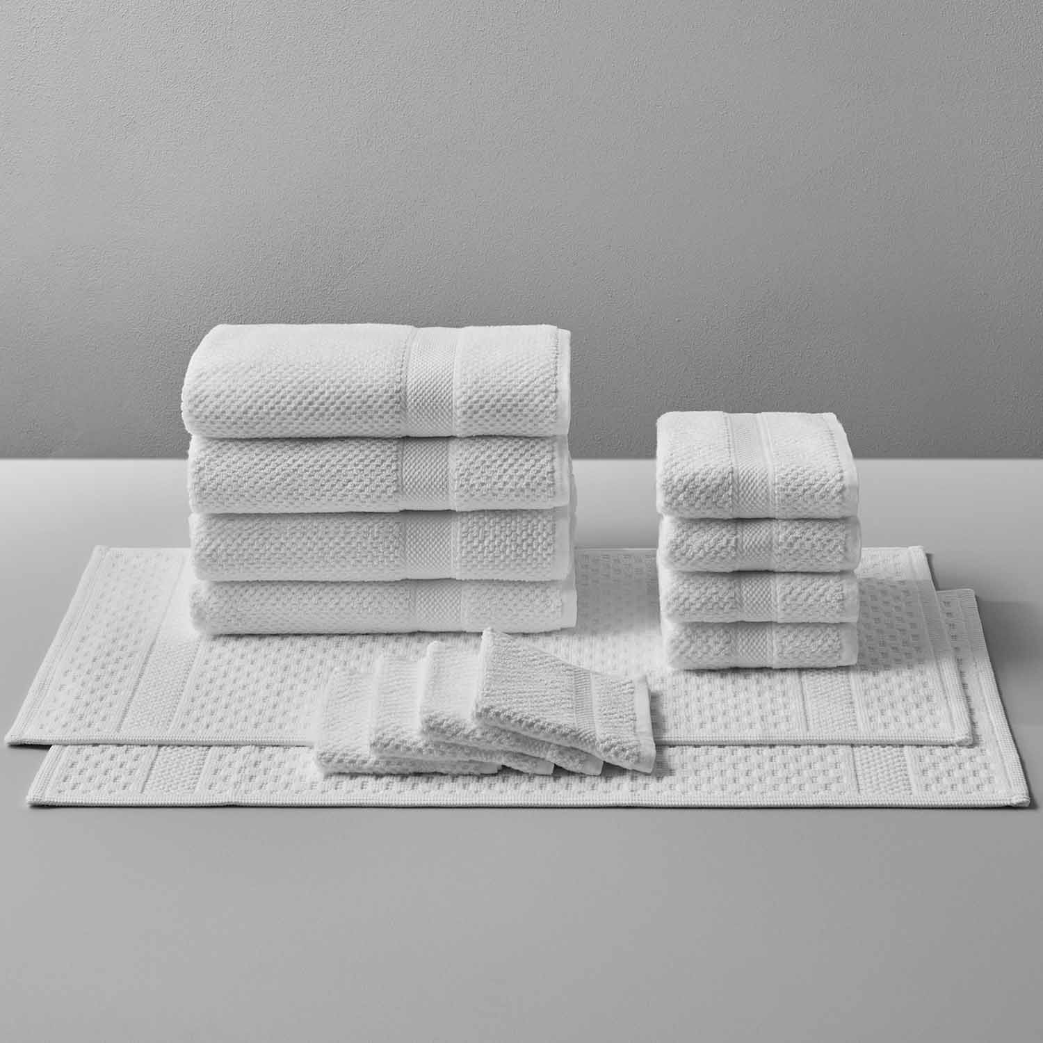 Set of luxurious Novotel towels made from 100% Brazilian cotton, arranged neatly on a table against a grey background.