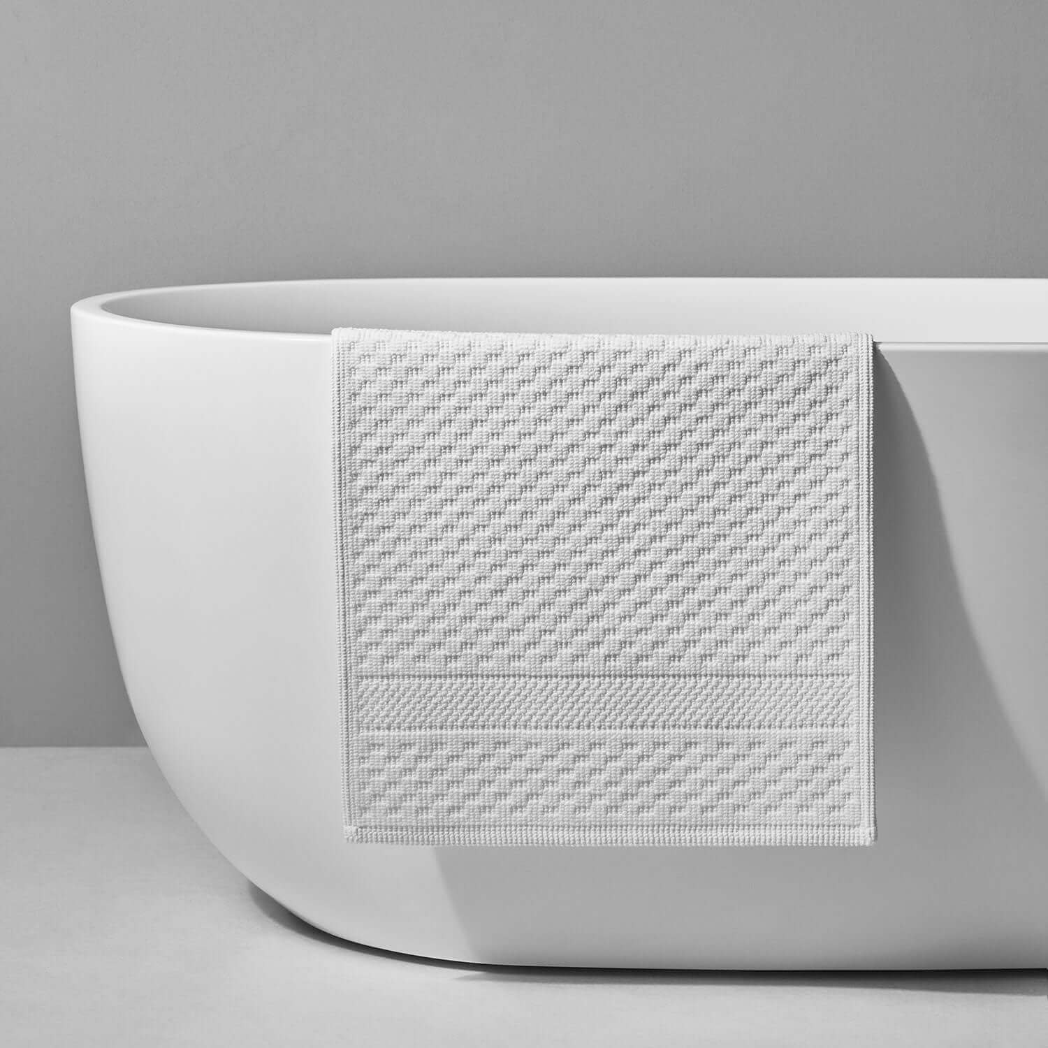 Luxurious white towel draped elegantly on a modern bathtub, showcasing textured craftsmanship for superior comfort.
