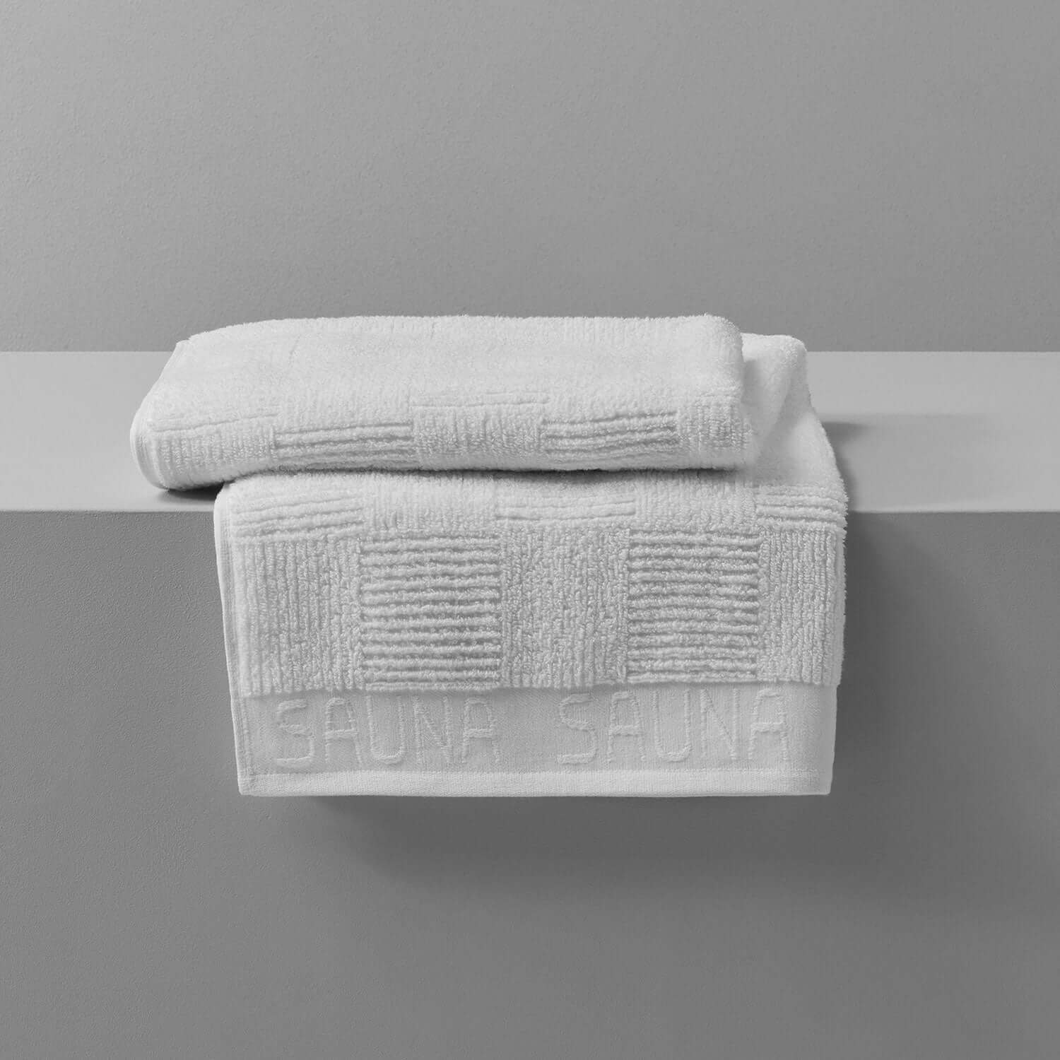 White sauna towels stacked on a shelf, designed for comfort and absorbency in sauna or steam room settings.