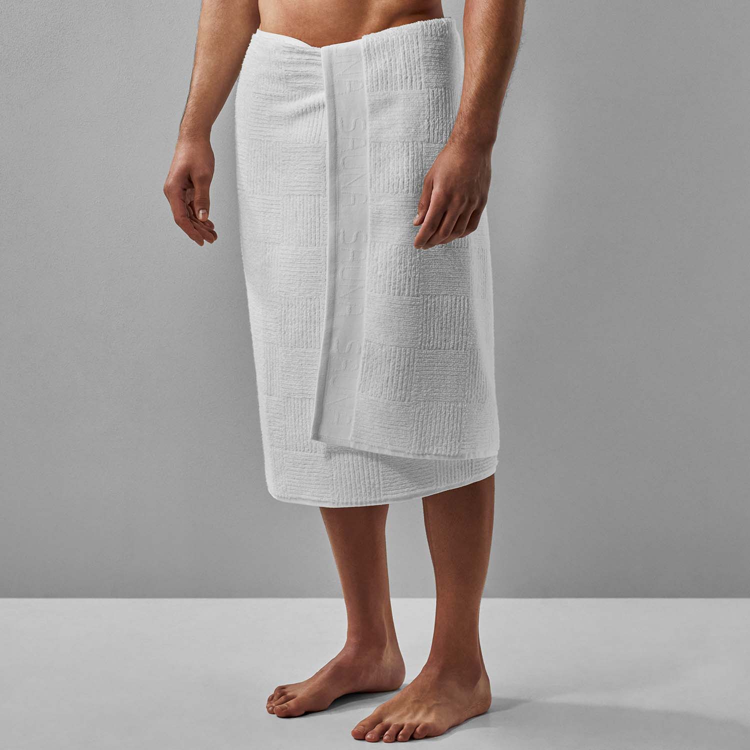 White sauna towel wrapped around a man, showcasing its plush design, absorbency, and comfort for relaxation.