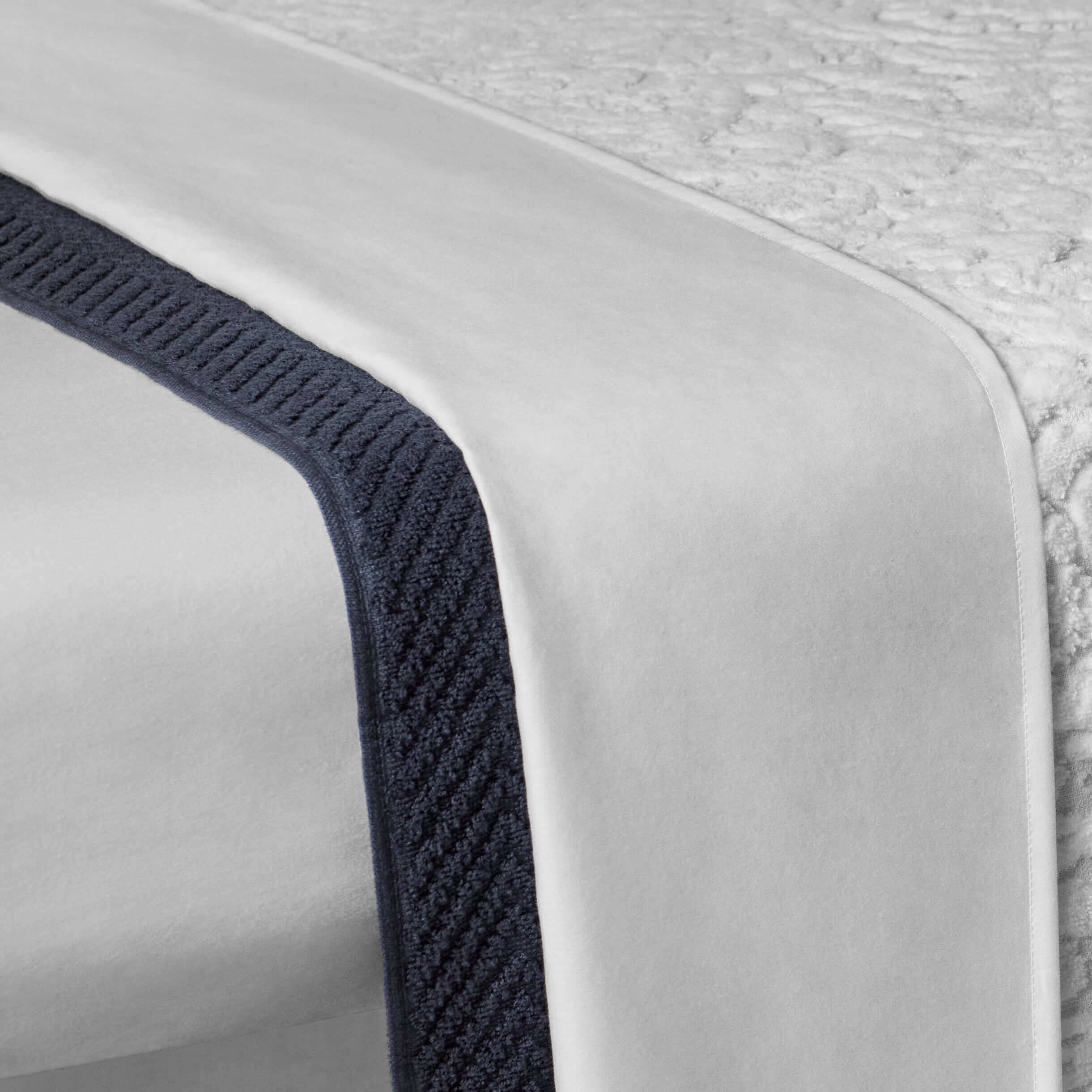 Elegant fitted sheet in white, featuring a sleek navy trim, ideal for luxurious bedding and spa-like comfort.