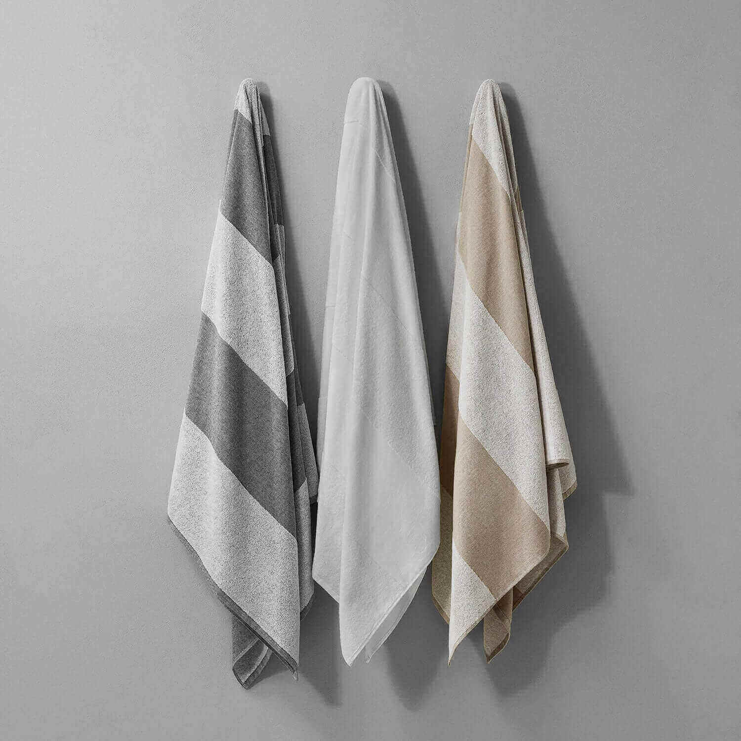SOL Striped Towels in gray, white, and beige hanging on a wall, perfect for beach or gym use.