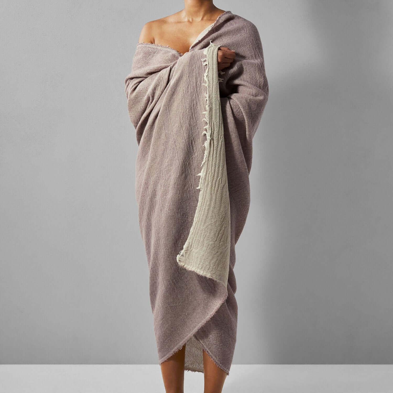 Woman wrapped in a reversible mauve Merino throw, showcasing fine Italian wool craftsmanship and light, elegant design.