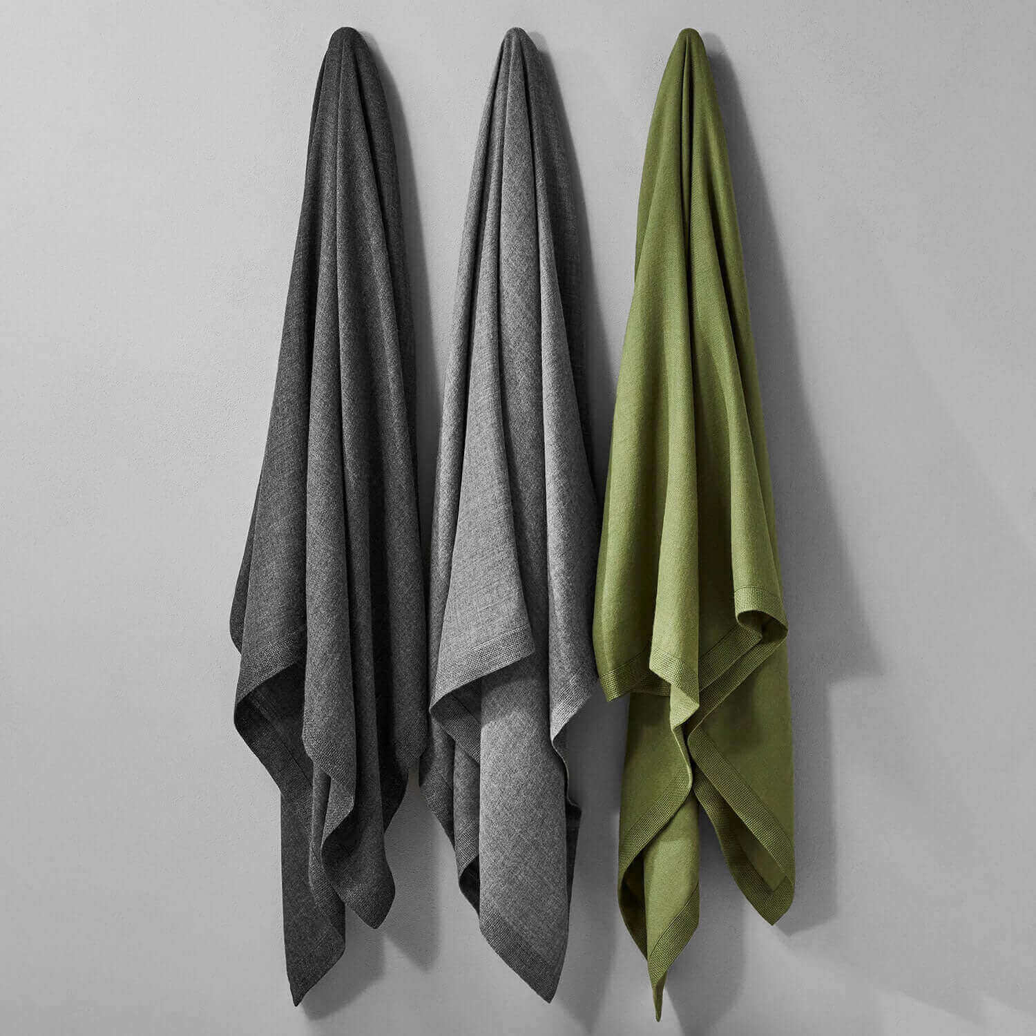 Three luxurious Baby Alpaca throws in charcoal gray and green, showcasing elegant softness and warmth on display.