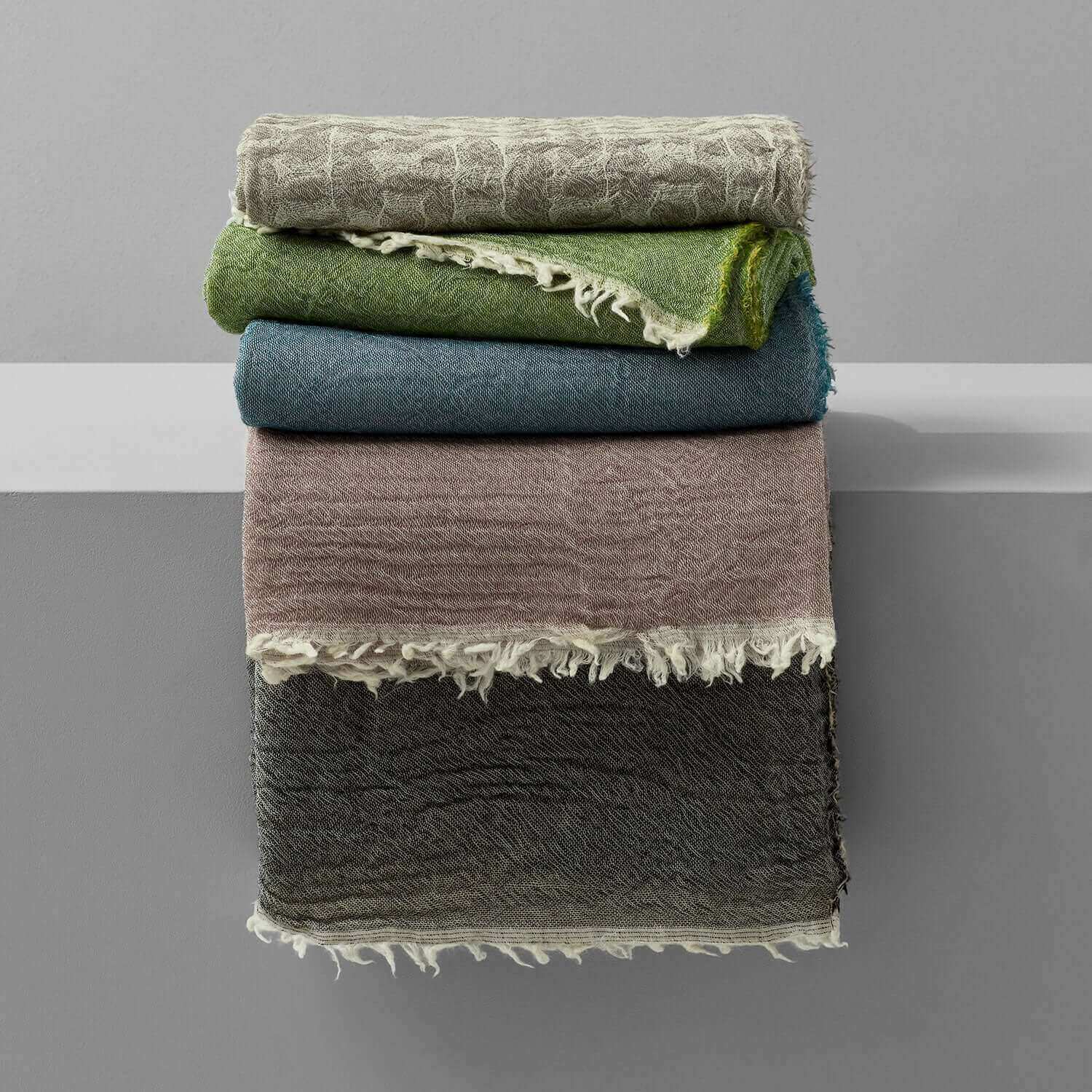 Merino wool throws in various colors stacked neatly, showcasing their intricate designs and soft textures.