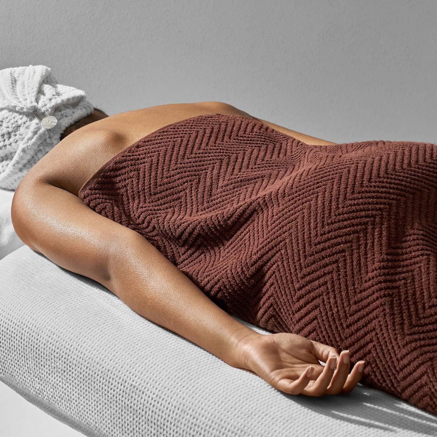 Luxurious brown towel with herringbone pattern draped elegantly over a relaxed individual, showcasing stylish spa décor.