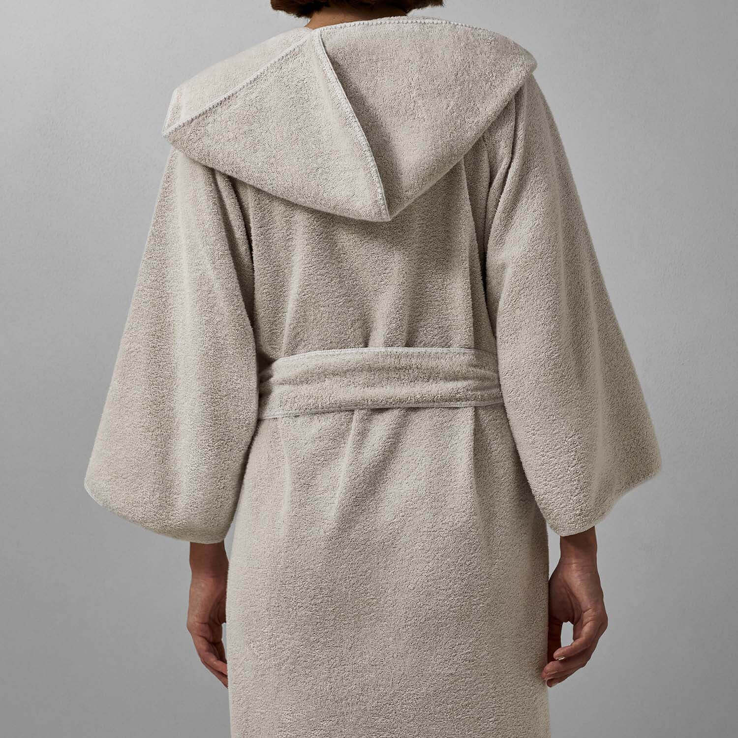 Back view of a plush, light grey hooded robe showcasing a self-tie belt and elegant rounded finishes.