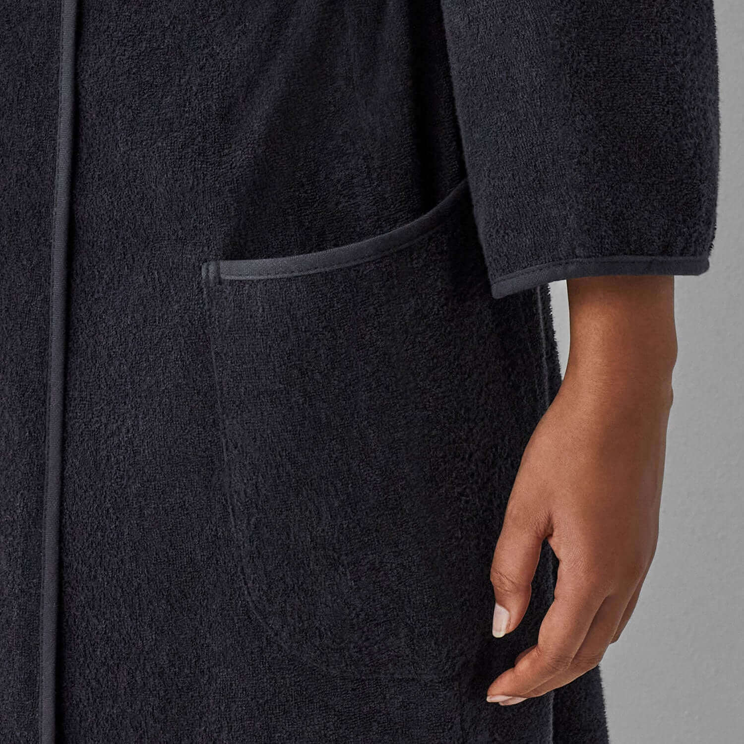 Close-up of a hand resting on the pocket of a luxurious black Wabi Sabi robe, illustrating minimalist design and sustainable elegance.
