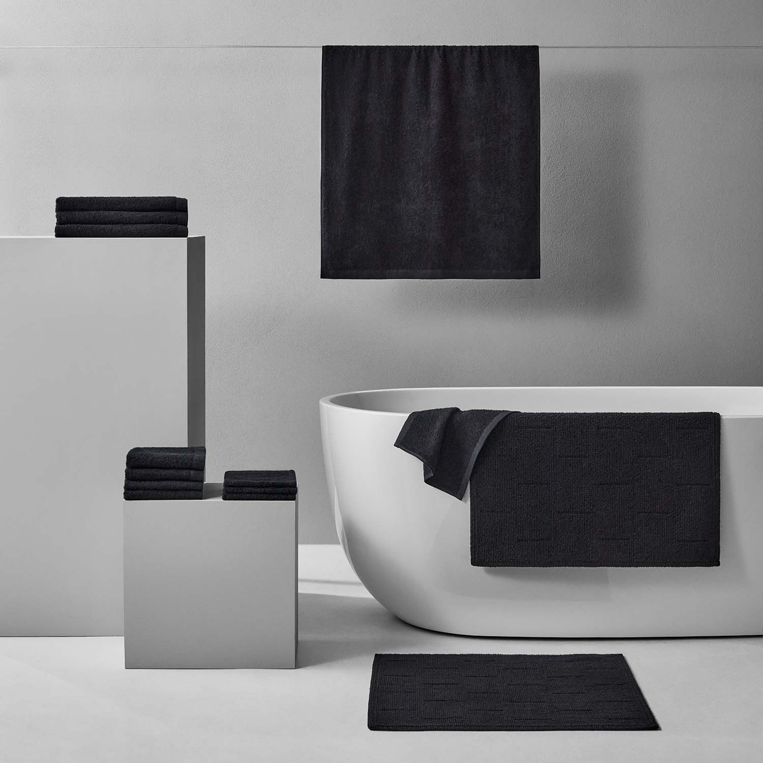 Wabi Sabi Bath Bundle in black, featuring minimalist towels and mats arranged elegantly around a modern tub.