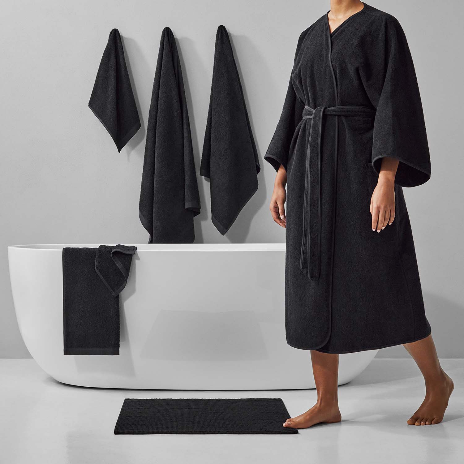 Person in a black bathrobe standing by a modern bathtub, showcasing luxurious towels and a stylish bathroom setting.