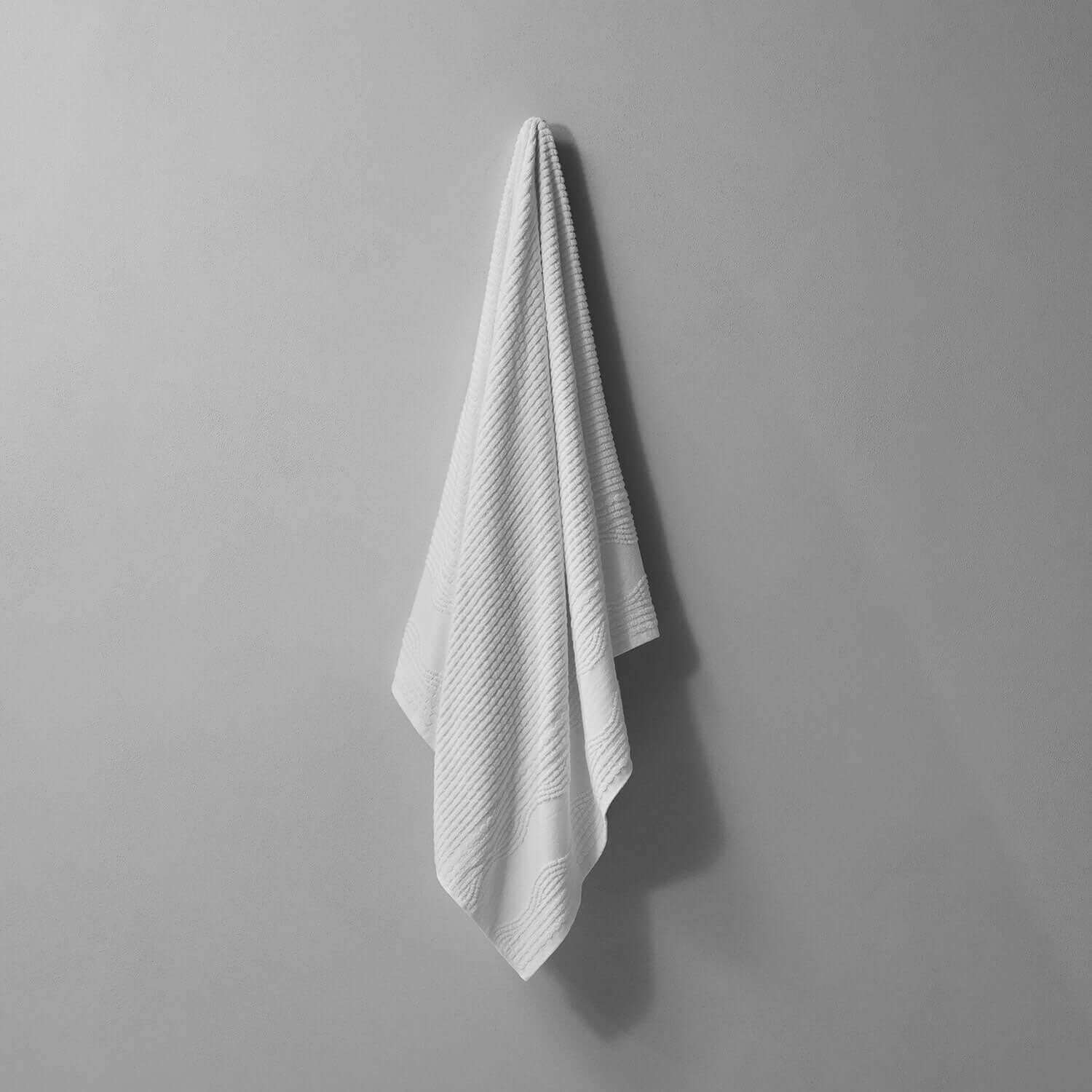 Lightweight pure cotton Wave Towel hanging against a wall, perfect for poolside use and quick drying after water activities.