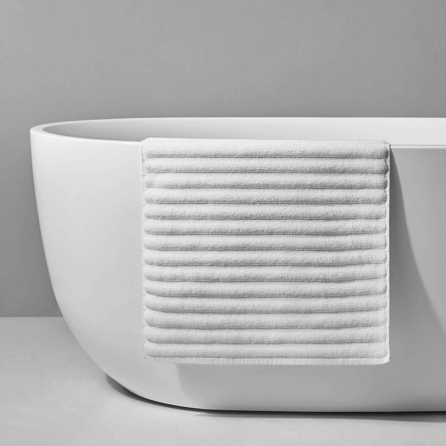 Stylish white cotton Wave Mat draped over a modern bathtub, perfect for luxurious bathroom comfort and safety.