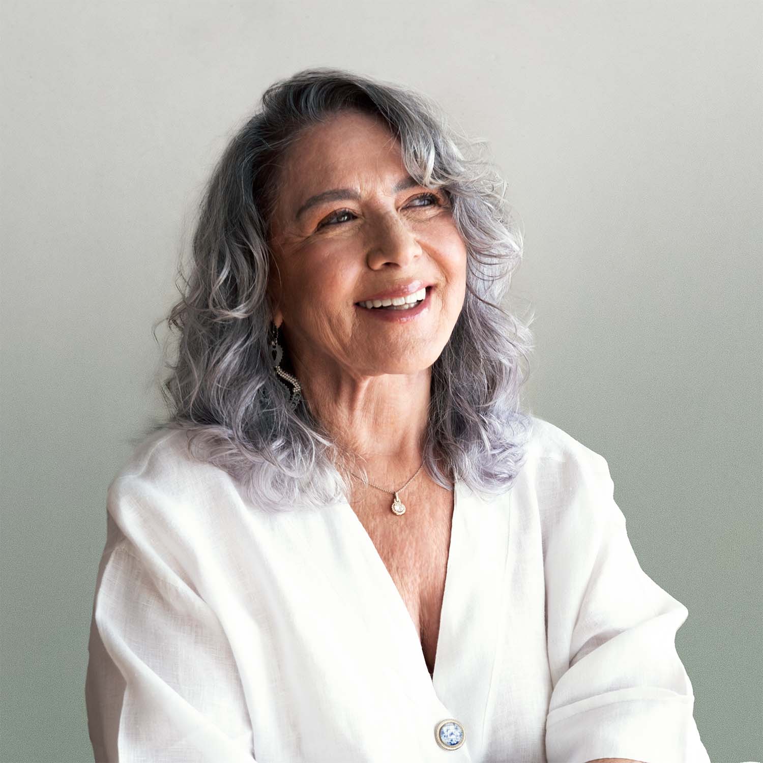 Smiling older woman with silver hair wearing a white blouse, exuding warmth and happiness against a soft background.