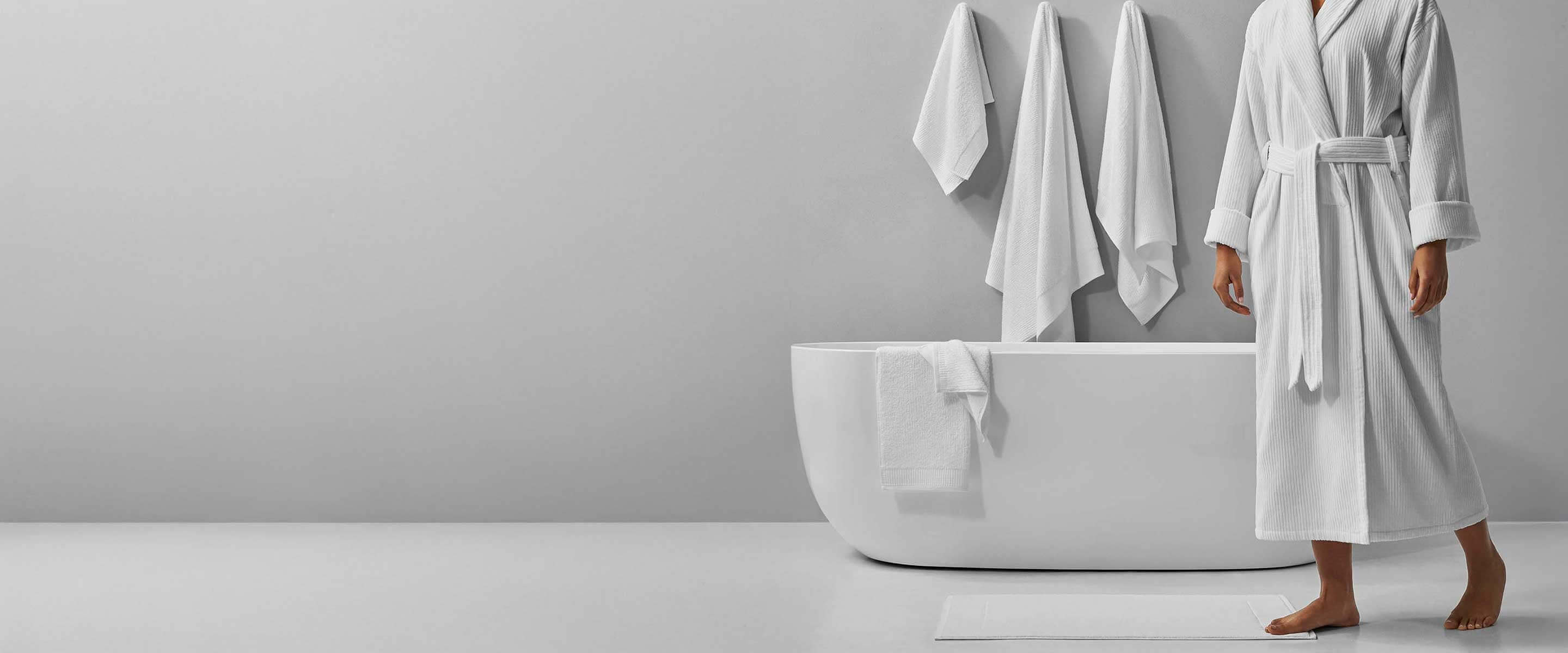 Elegant bathroom scene featuring a person in a white robe next to a modern bathtub and hanging towels.