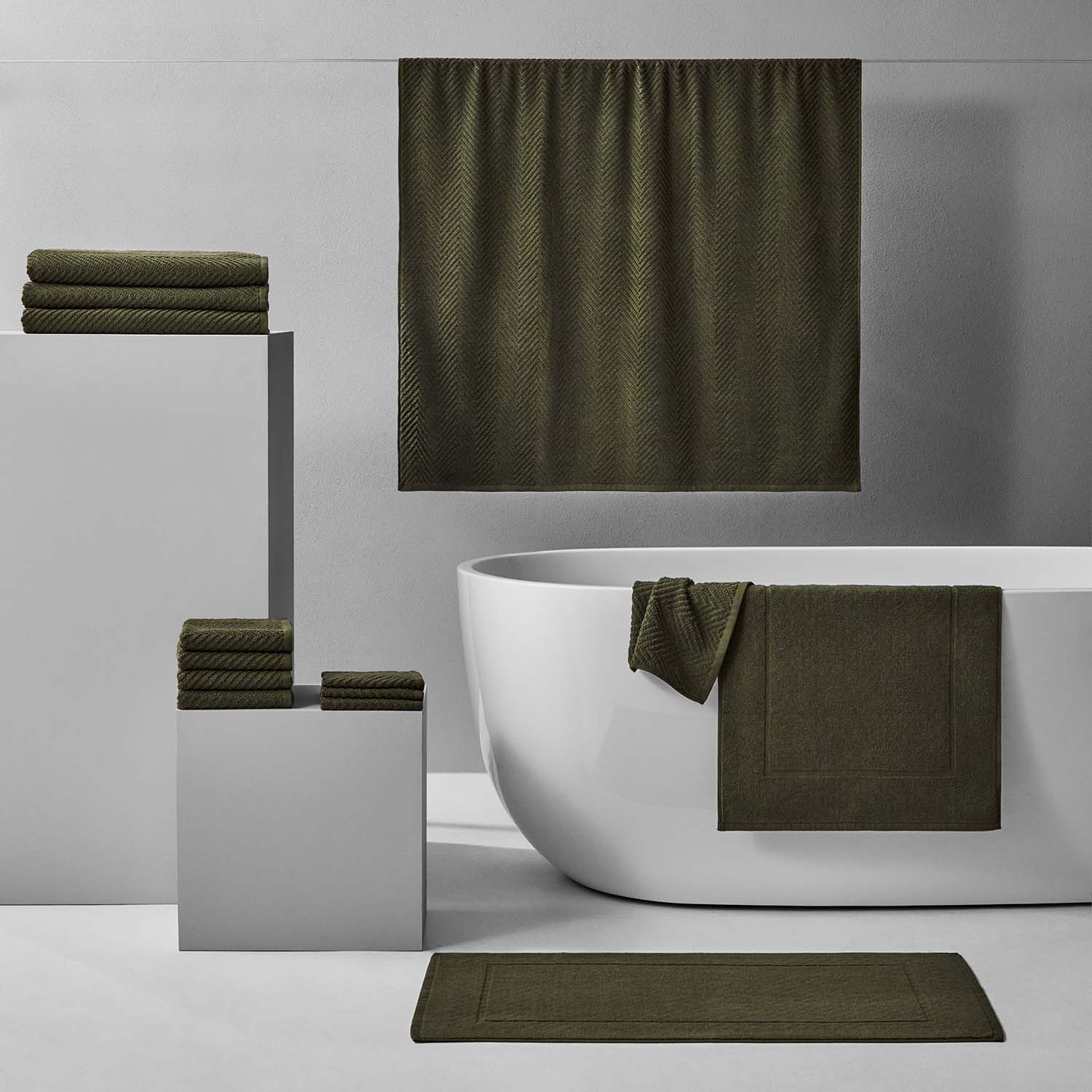 Treatment Bath Bundle Olive: elegant green towels and bathmat arranged around a modern white tub for relaxation.