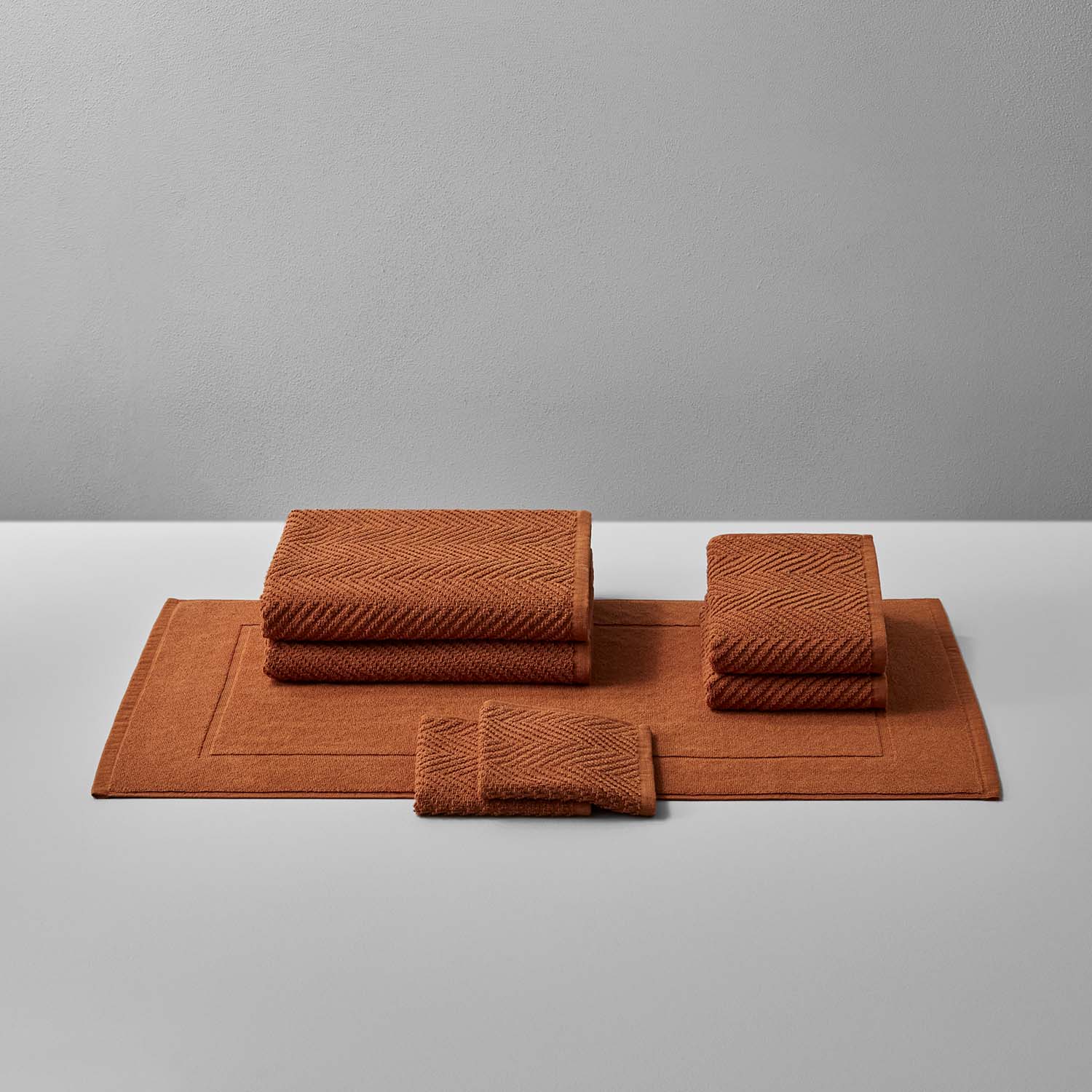 Warm earthy-tone treatment bath bundle featuring soft, textured towels and a mat designed for relaxation and care.