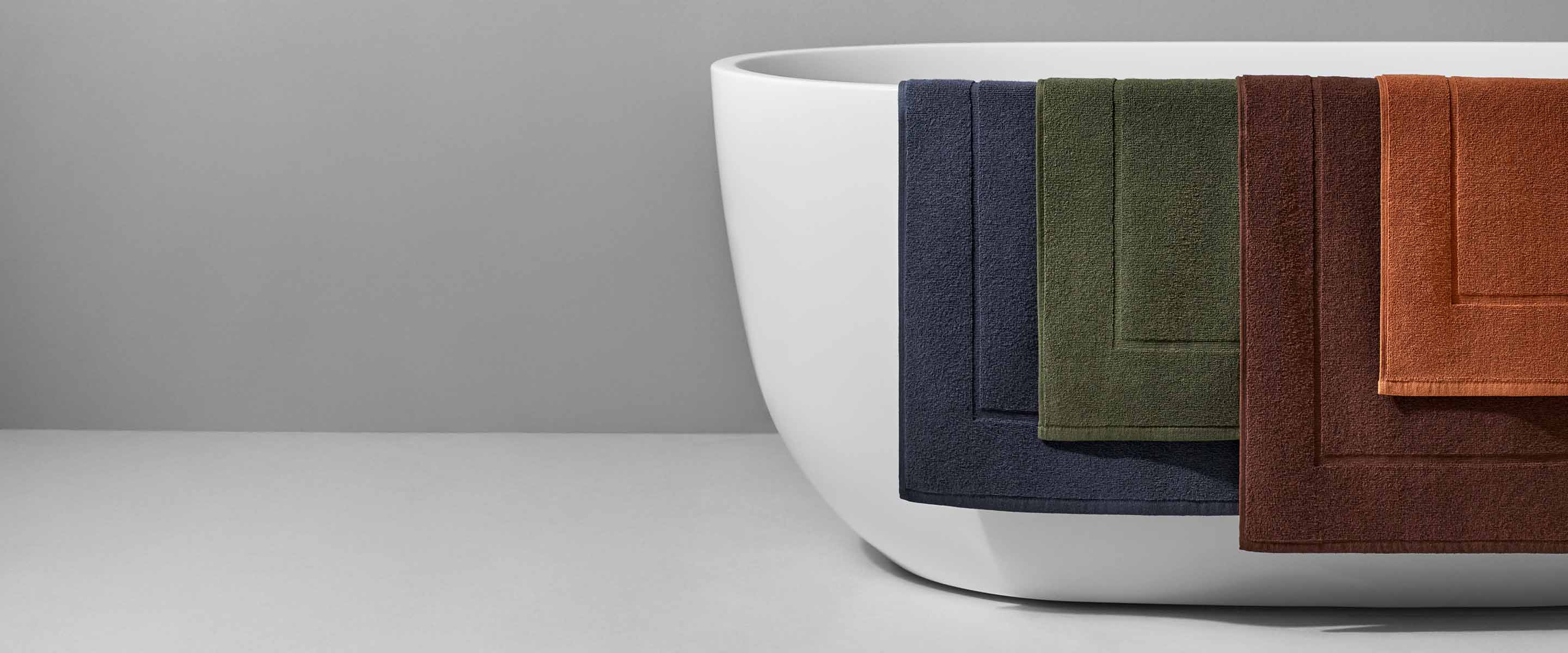 Elegant bathroom scene featuring textured towels in navy, green, and rust colors draped over a modern white bathtub.
