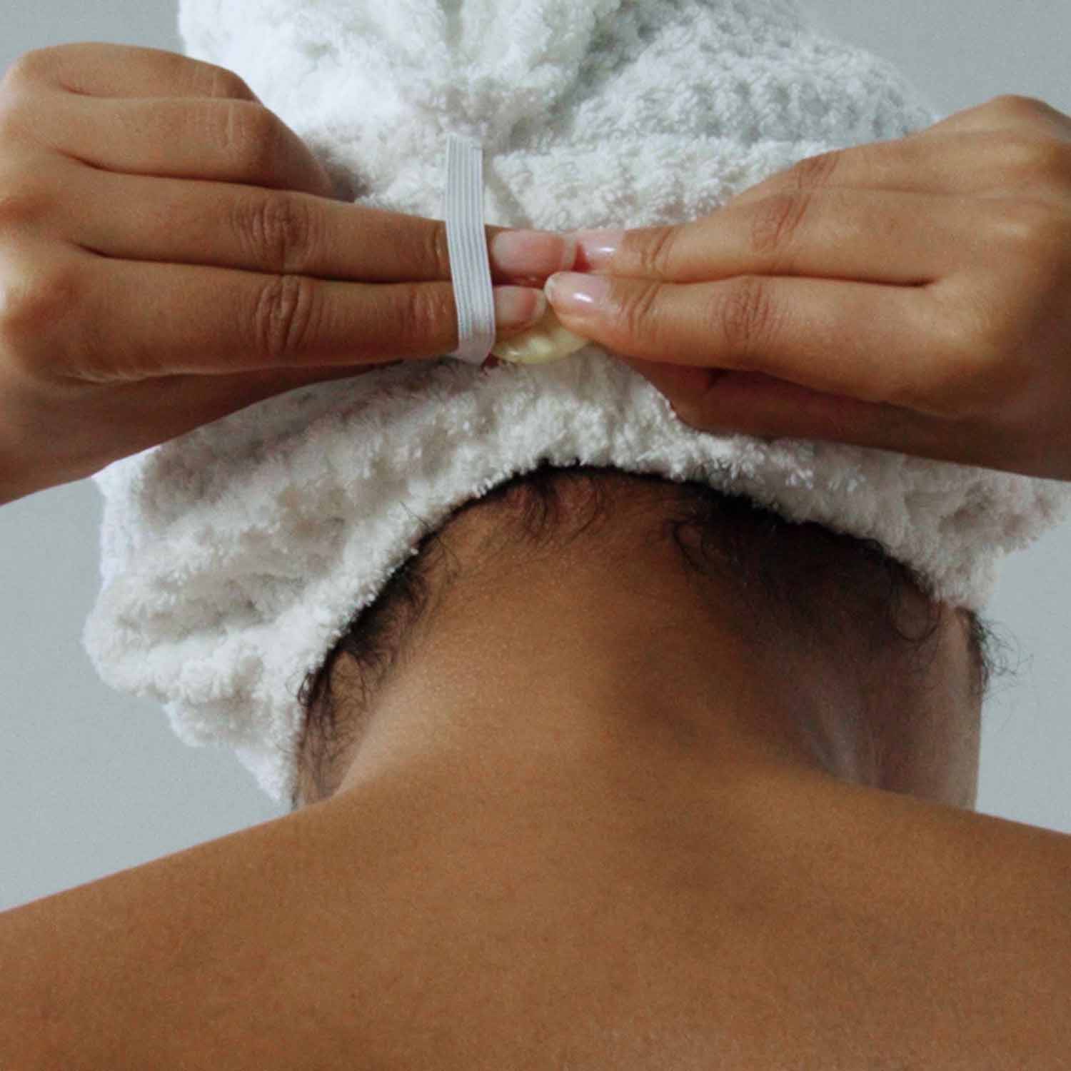 Person securing a plush white towel on their head after showering, showcasing convenience and style.