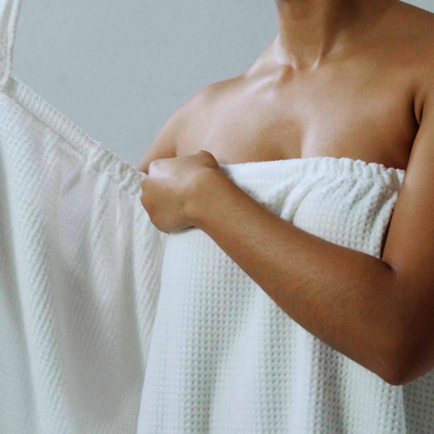 Close-up of a person holding a lightweight white velour body wrap, demonstrating adjustable unisex design for spa use.