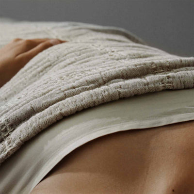 Close-up of a textured stone-beige stitch blanket draped over a person, showcasing its natural elegance and comfort.